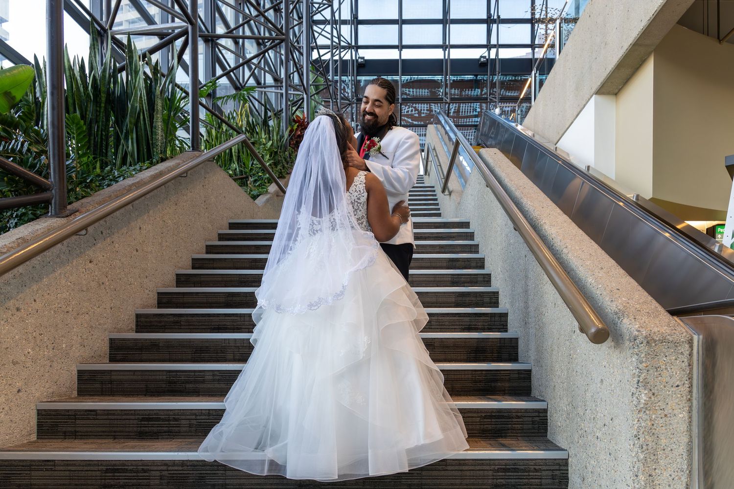 Bride in a white gown and veil posing with groom on an outdoor staircase during wedding photography.