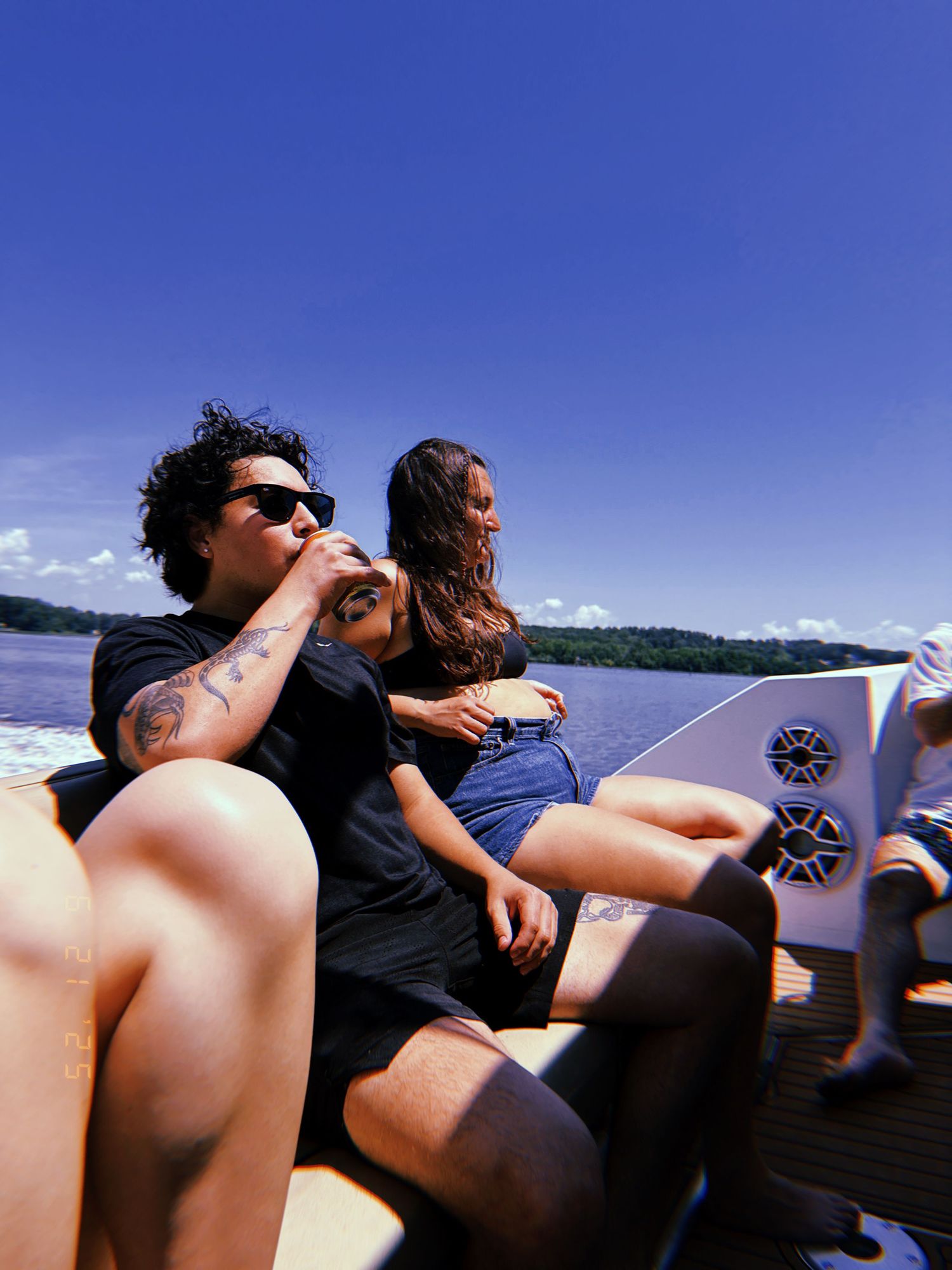 People lounging on the back of a boat cruising across a lake on a sunny summer day.