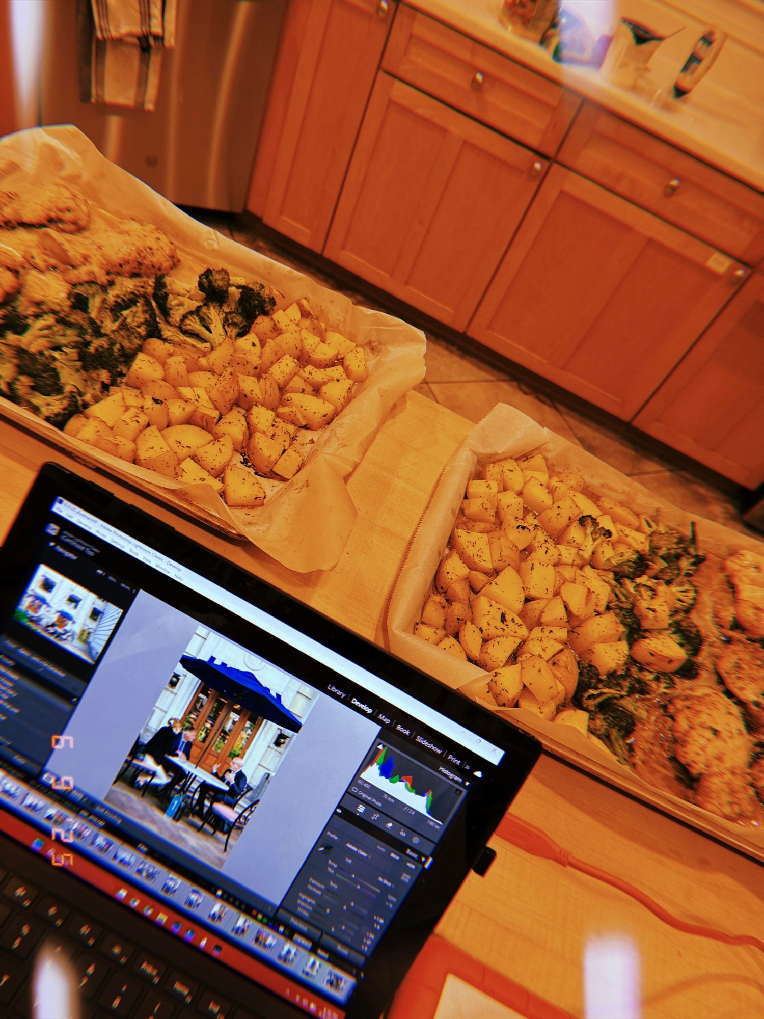 A laptop displays video editing software next to piles of fried chicken wings and other appetizers on brown paper.