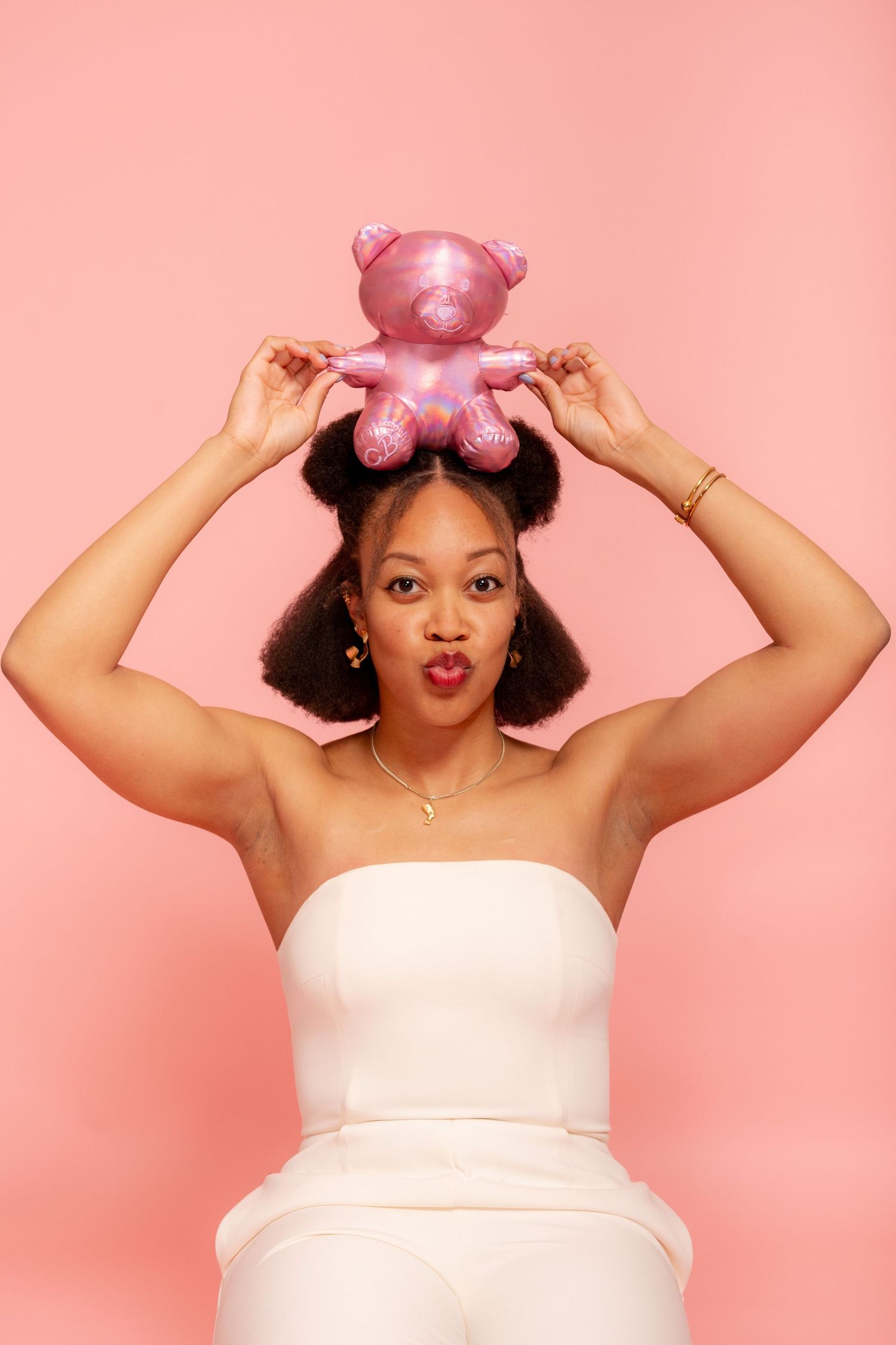 Four connected photos show someone in a white top posing playfully with a pink sleeping mask against a pink background.