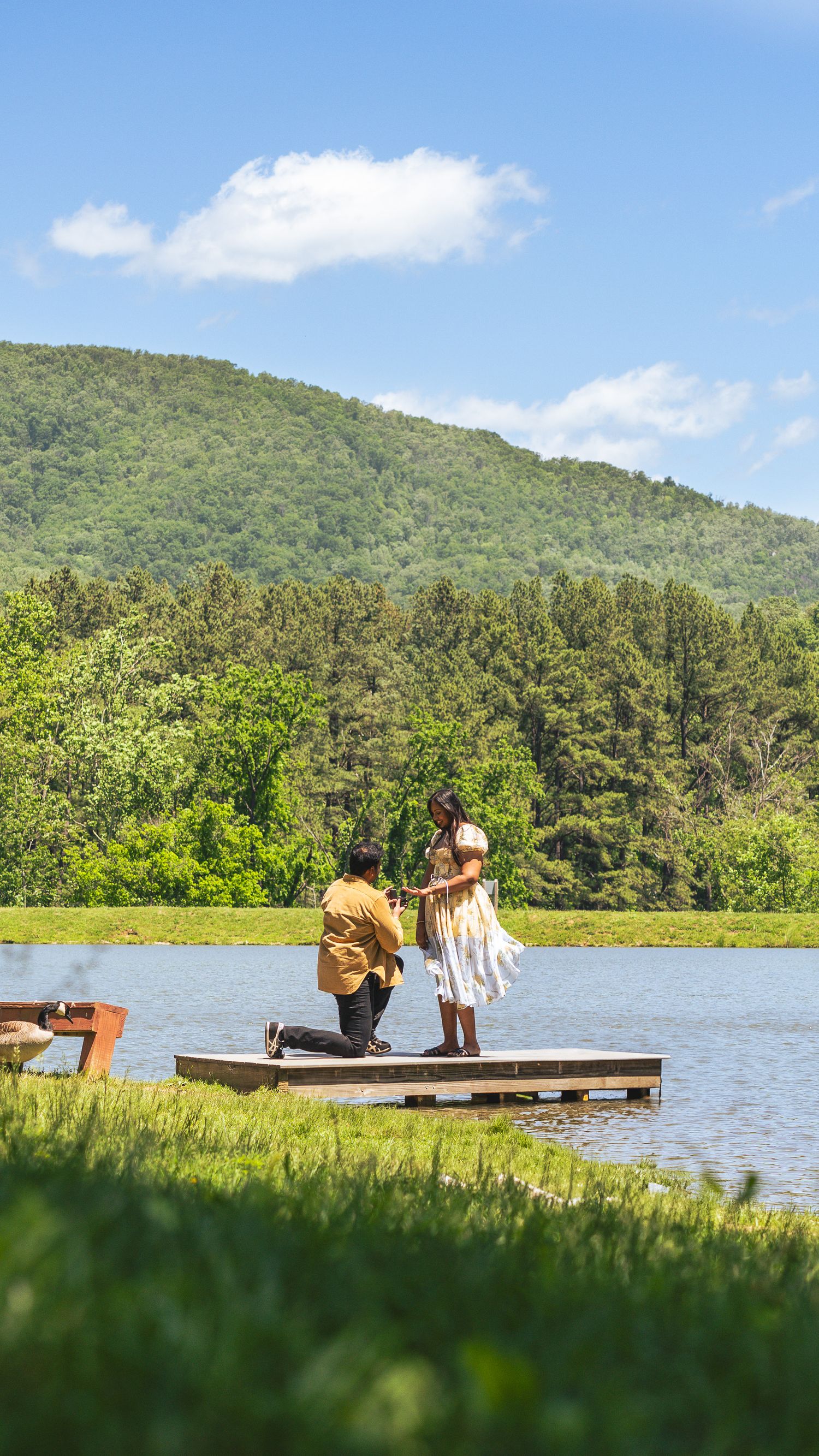 Two people relax on a wooden dock overlooking a serene mountain lake on a sunny summer day.