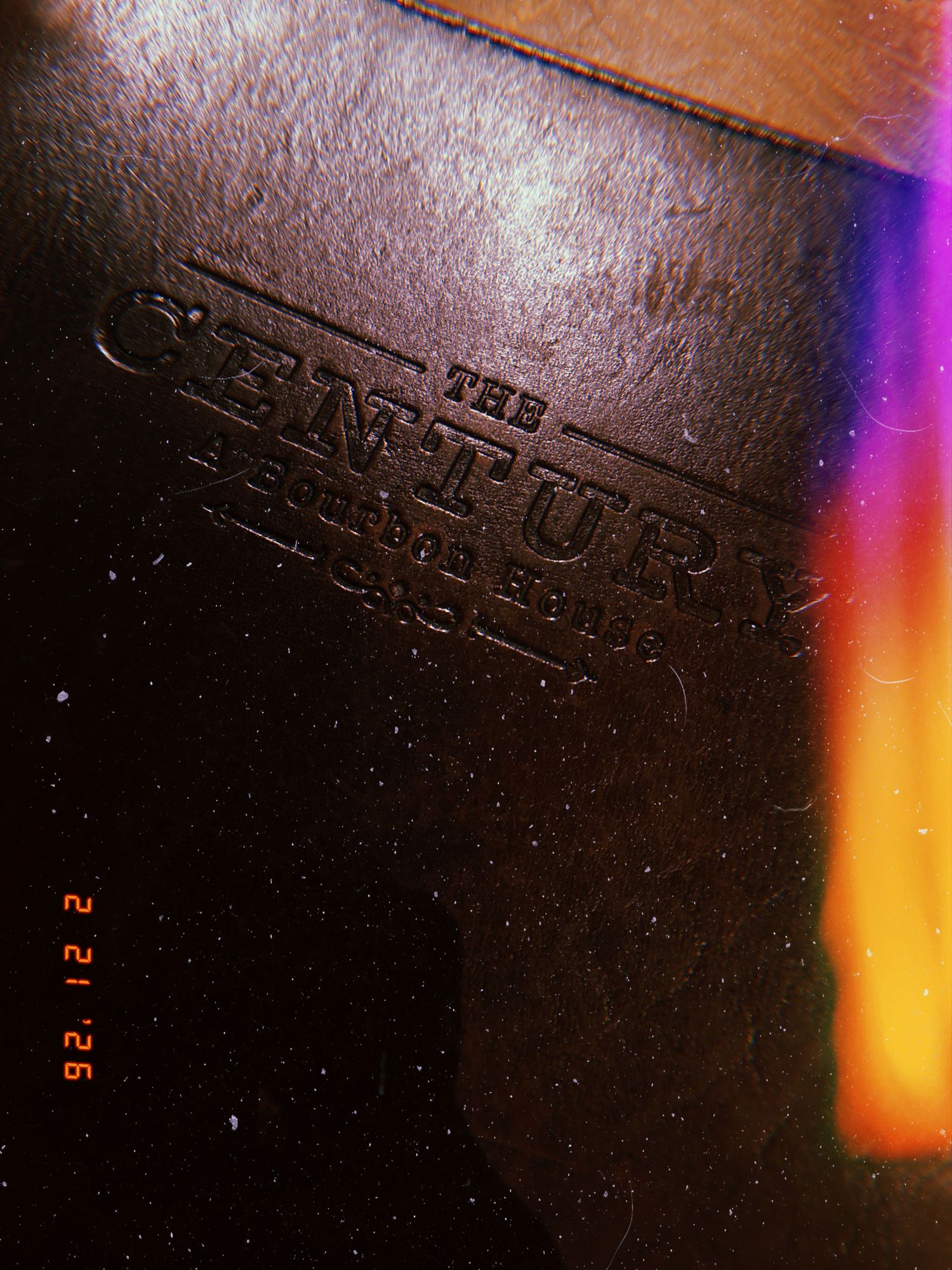Close-up view of embossed text on dark leather or paper surface with colorful light reflection in the corner.