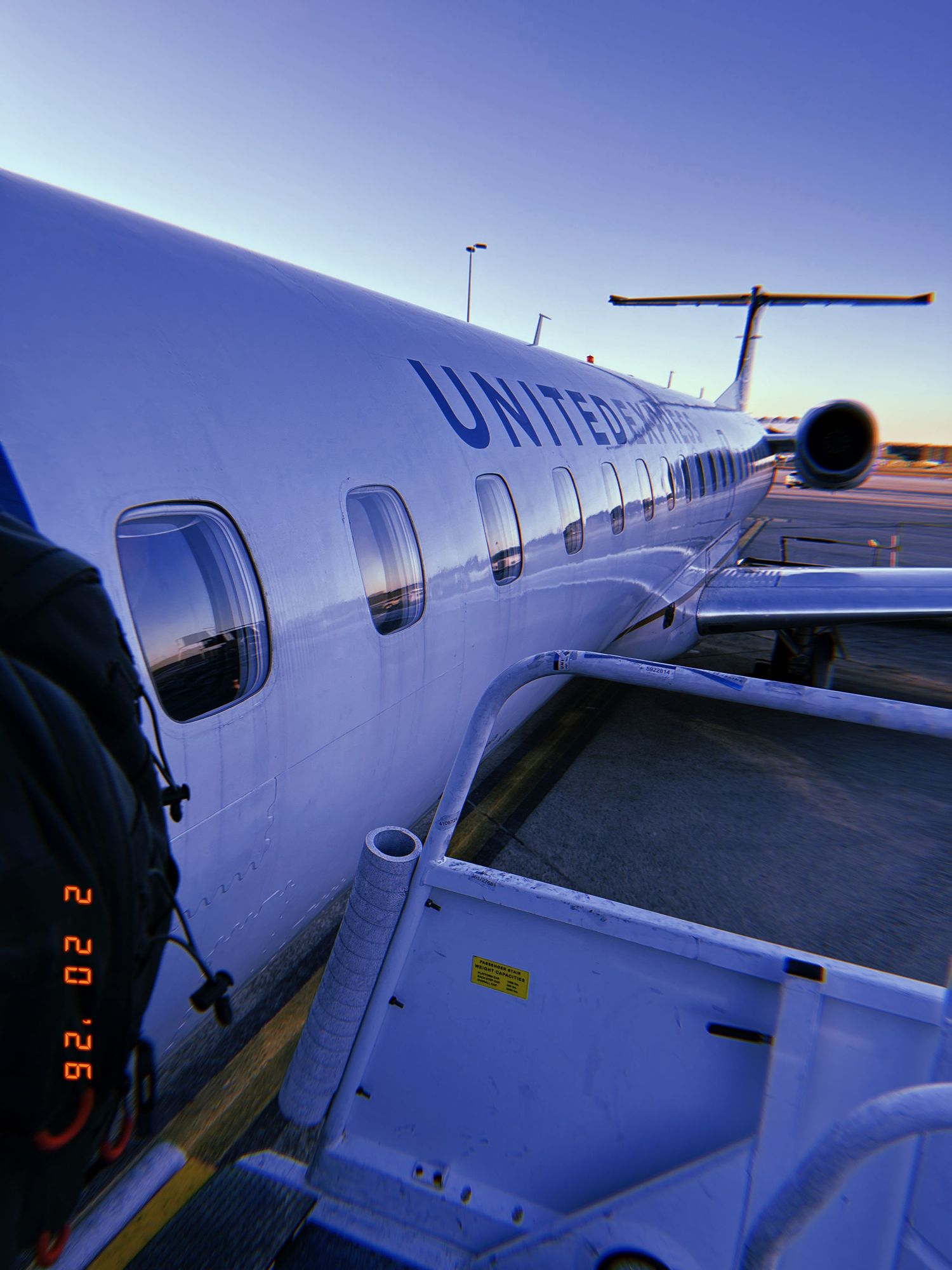 A United Airlines regional jet parked at the gate with passenger windows and loading equipment visible at sunset.