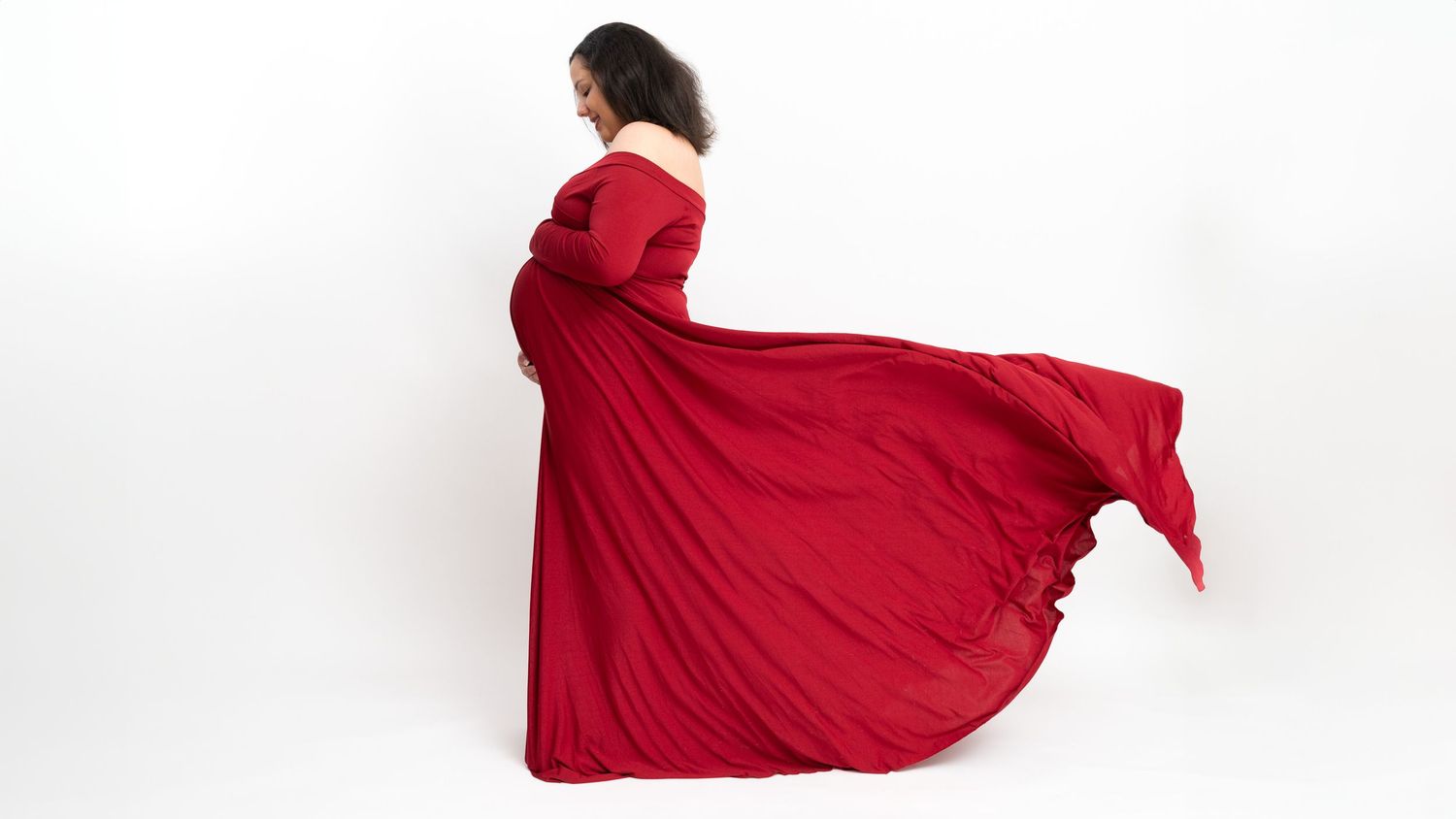 Woman in flowing red dress dances gracefully across white studio floor creating elegant movement sequence.