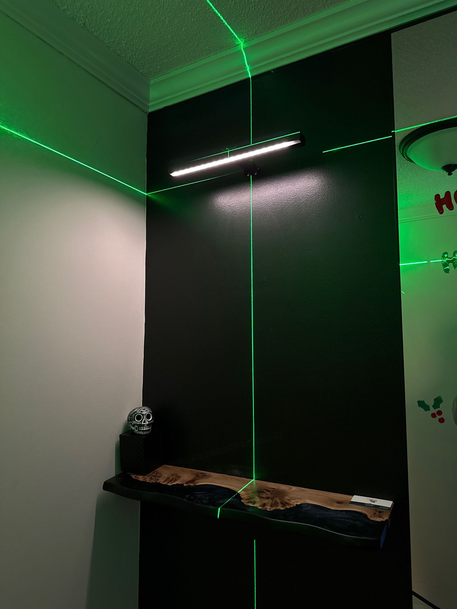 Green laser beam intersects with a floating wooden shelf in a dark room illuminated by fluorescent lighting.