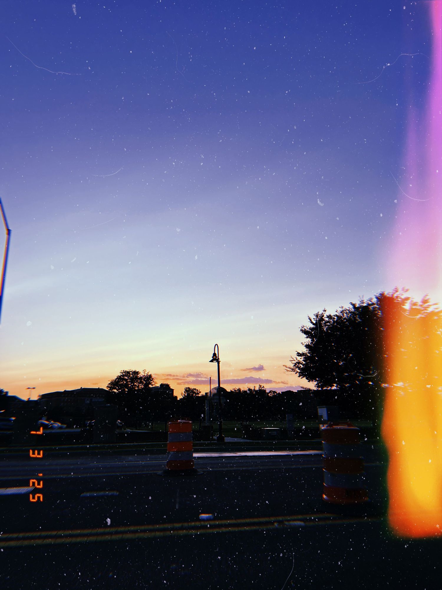 A twilight sky with orange light leaks captured on film, showing silhouettes of trees and a streetlight at dusk.