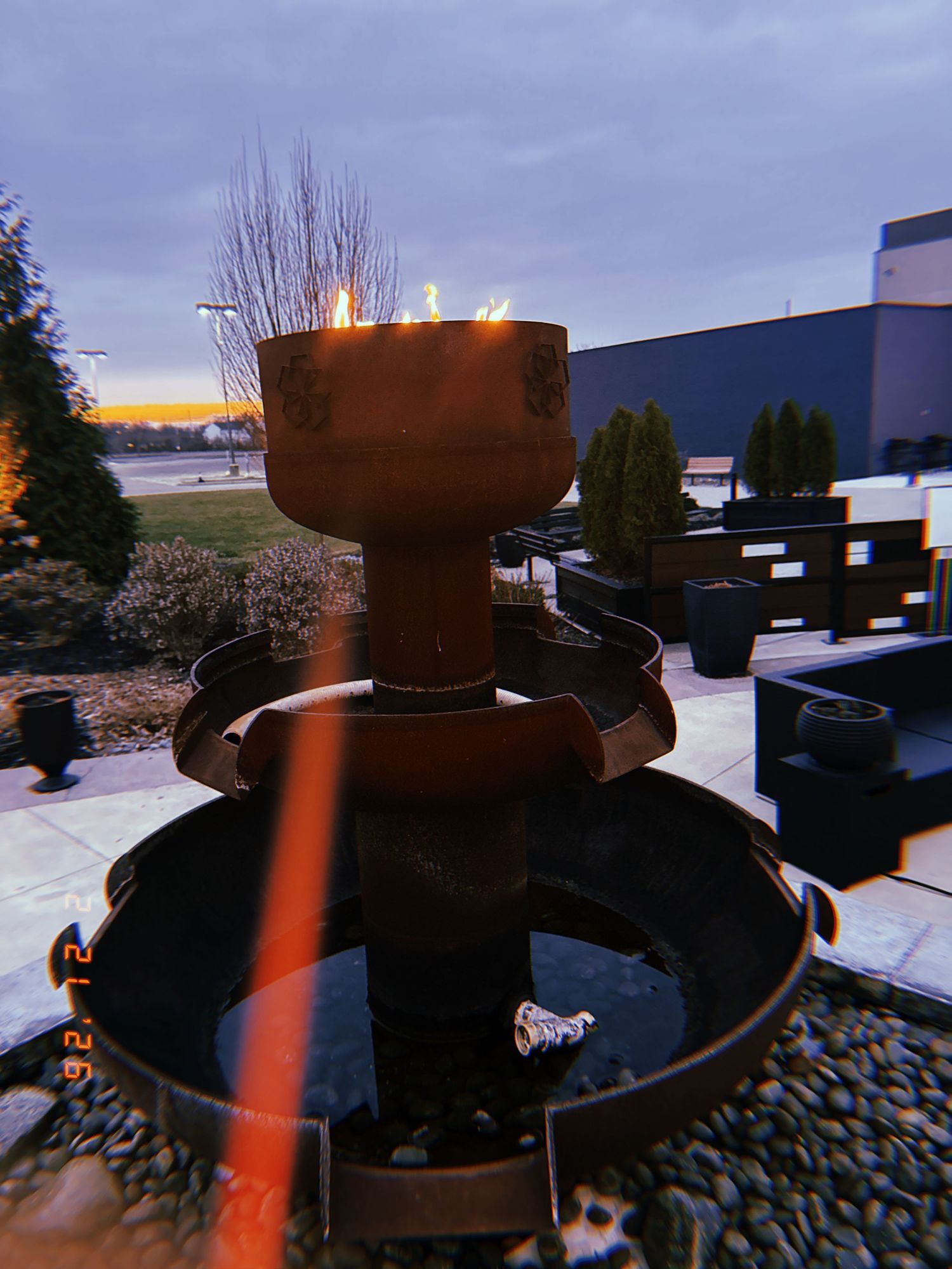 A series of outdoor fire pits with glowing flames against a dusky sky create a cozy ambiance on a patio setting.