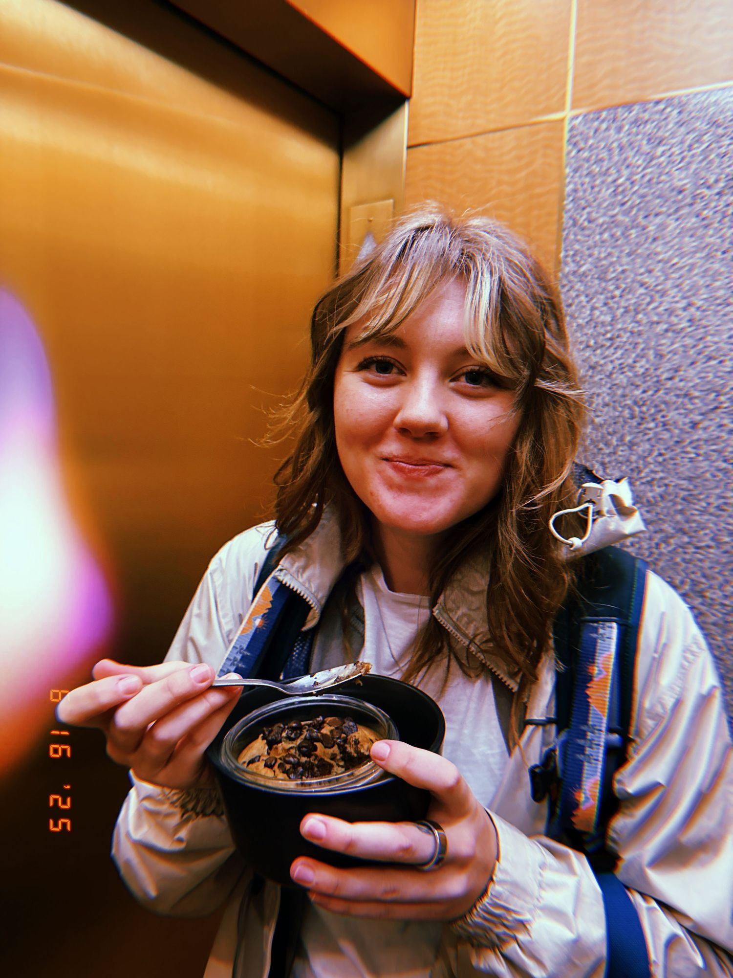 Someone eating from a black bowl while wearing a light colored jacket.