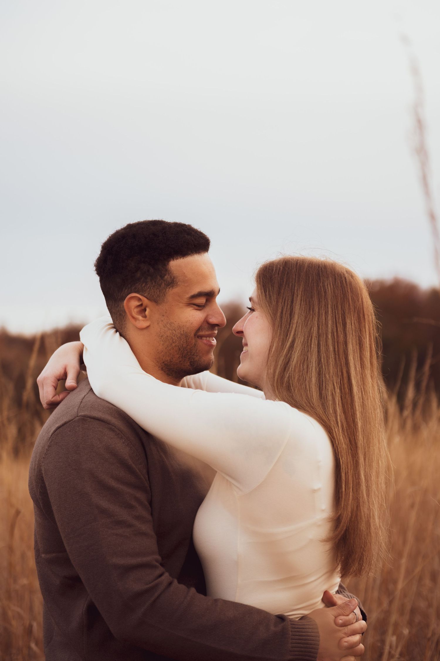 A romantic couple embraces and shares tender moments in a field of tall grass at sunset.