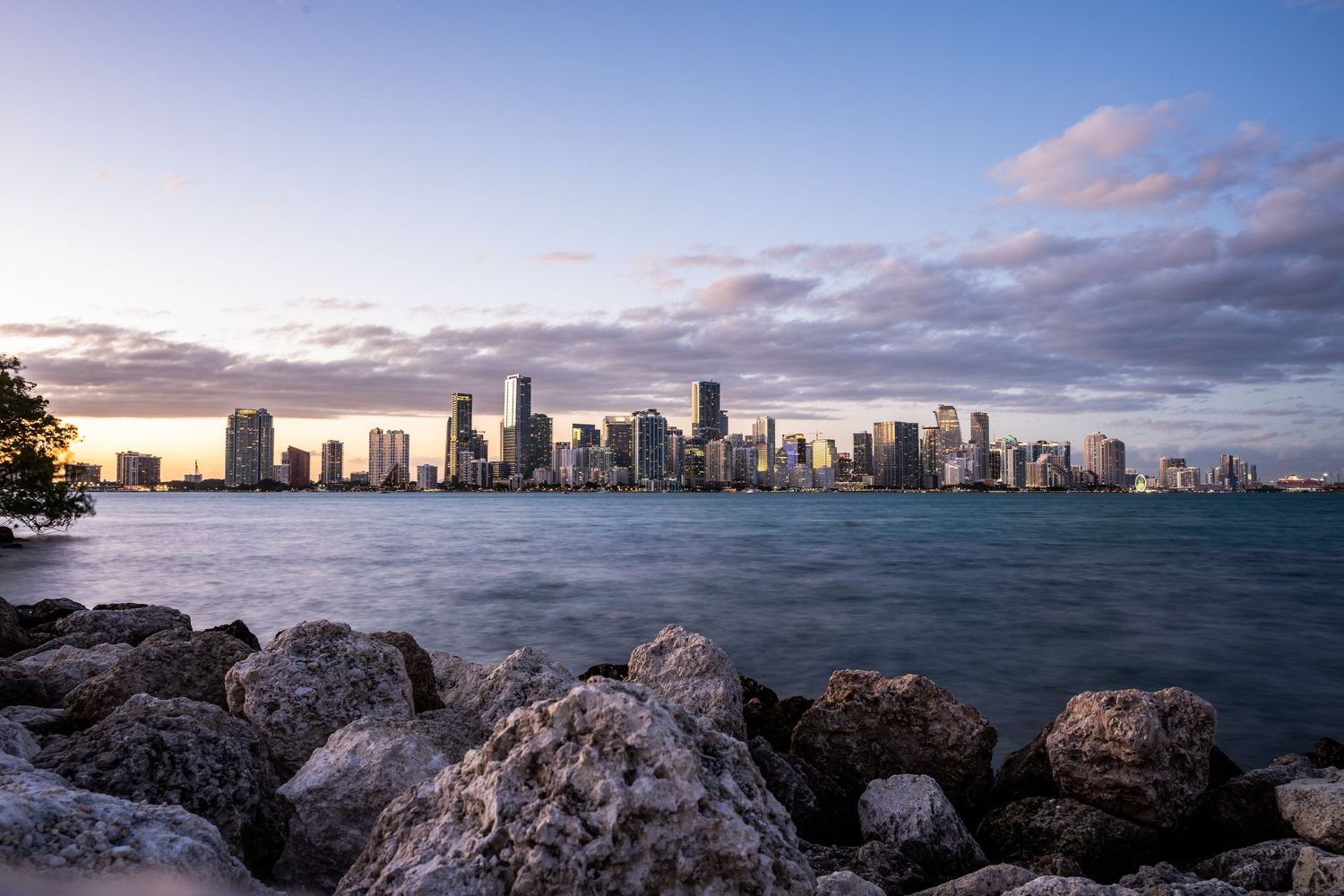 Panoramic cityscape of Miami skyline at sunset with ocean and dramatic clouds in the background.