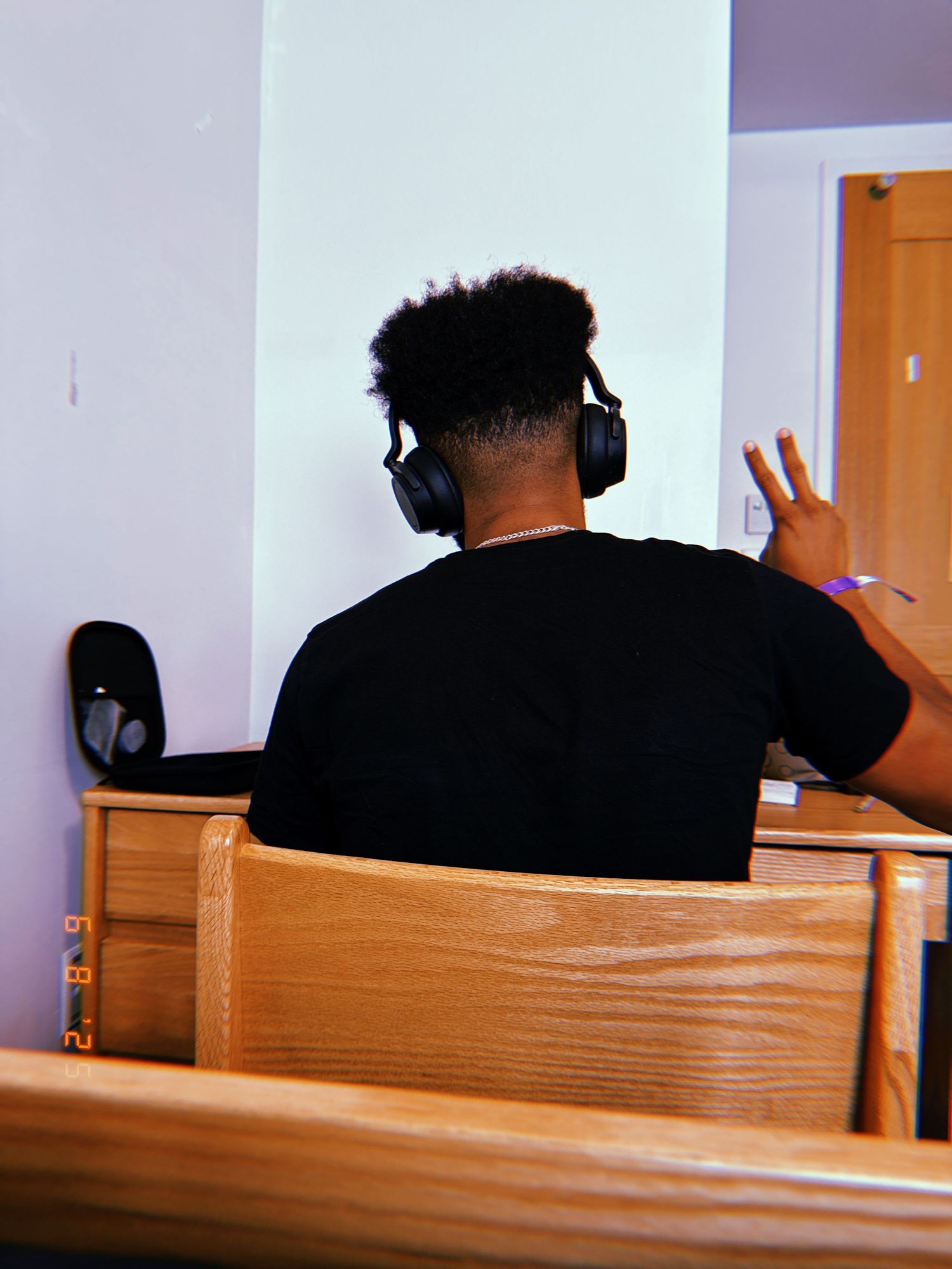 Someone wearing headphones sits in a wooden pew while working in front of a wall.
