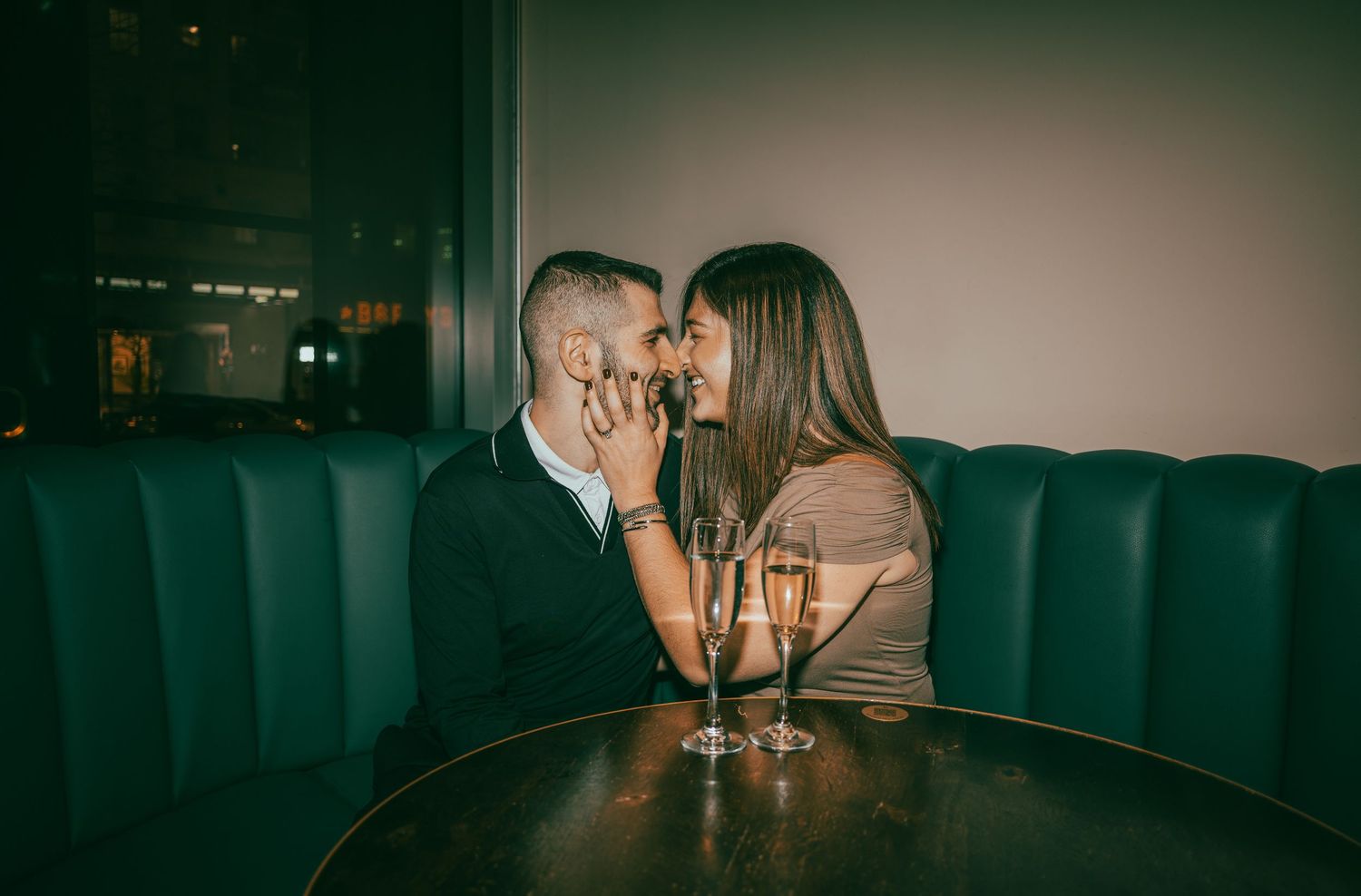A romantic couple shares intimate moments at a dimly lit restaurant table with wine glasses.