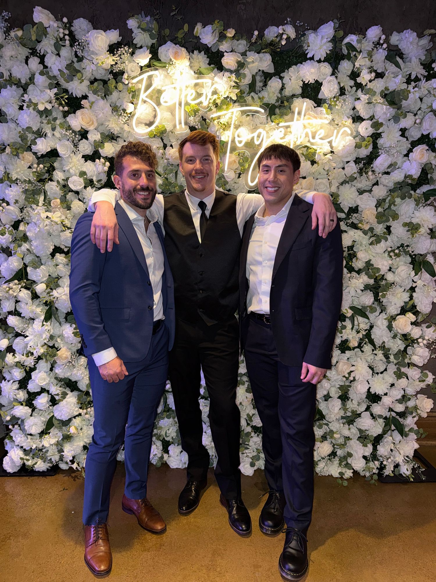 Group of friends posing together against a white floral backdrop at an elegant event.