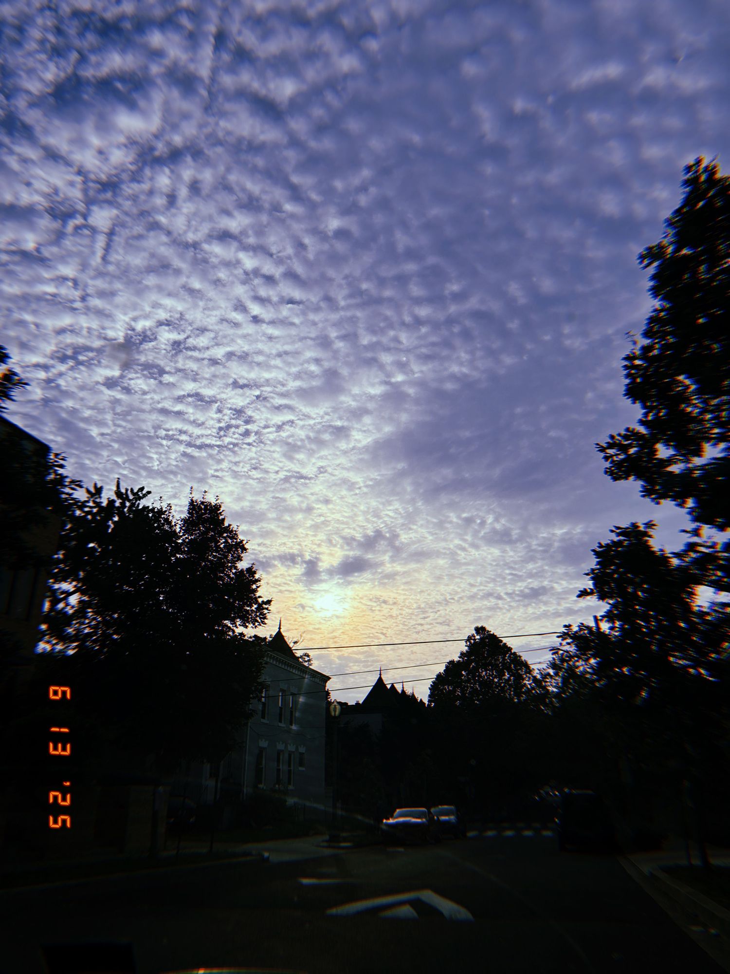 A dramatic altocumulus cloud formation fills the twilight sky above dark silhouettes of trees and buildings.