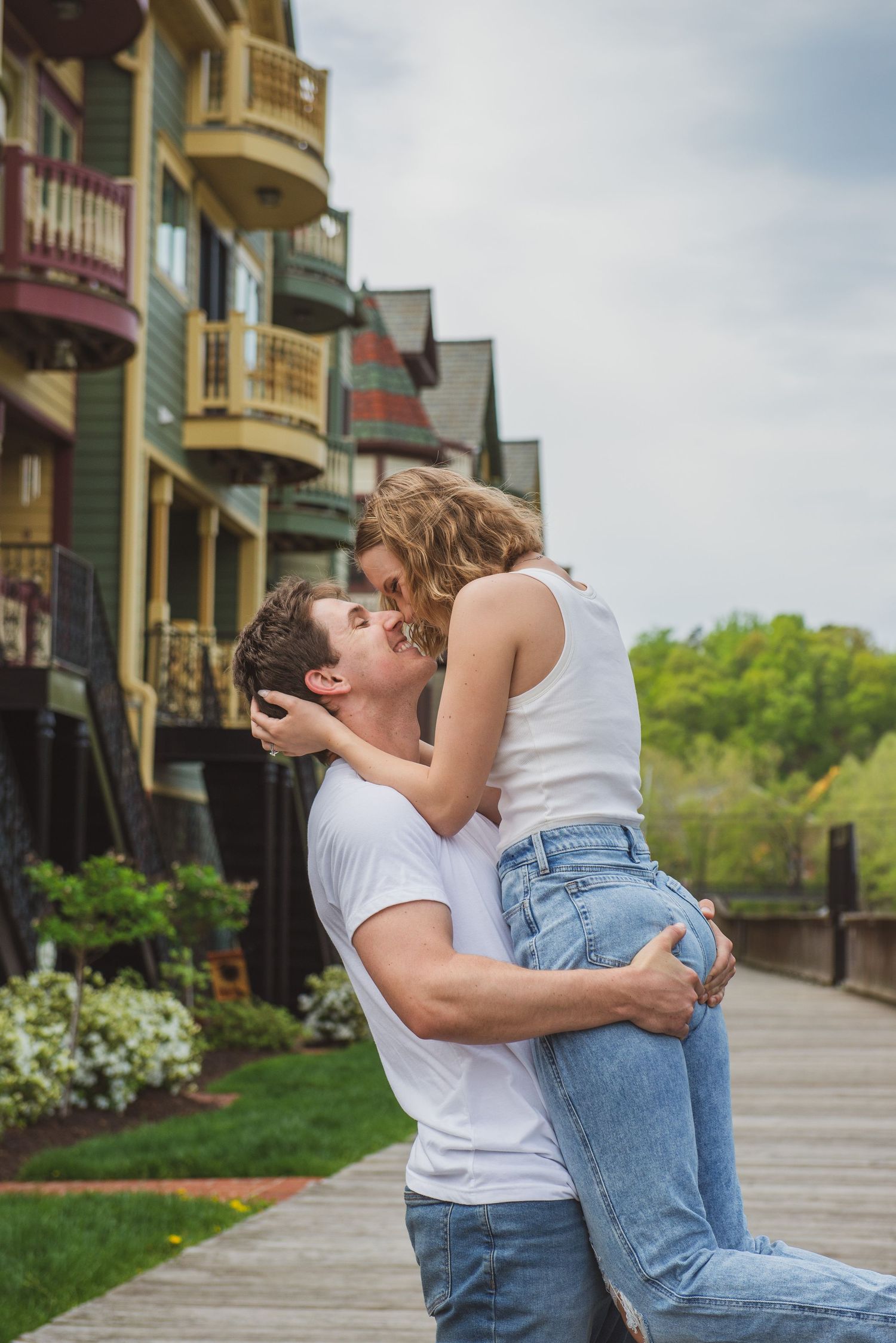 Romantic couple embracing on boardwalk near colorful townhouses.