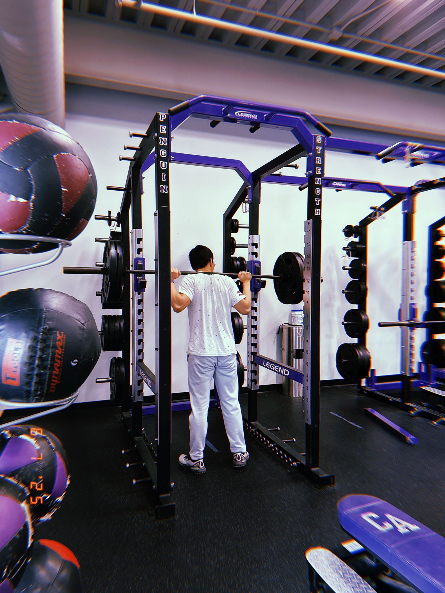 Modern fitness facility interior with multiple squat racks, training equipment and blue LED lighting accents.