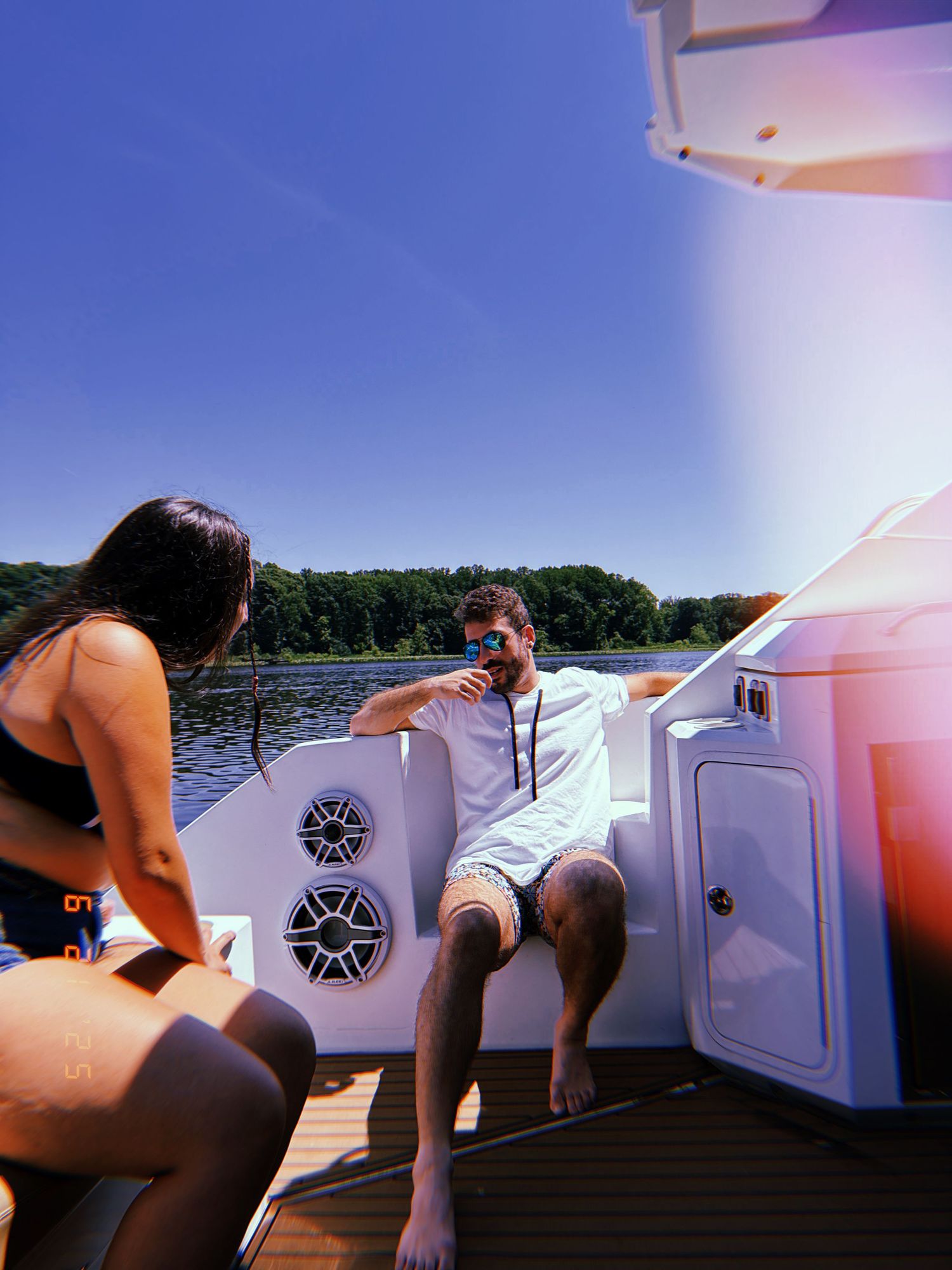 People relaxing on a boat deck with speakers and equipment on a sunny summer day at the lake.