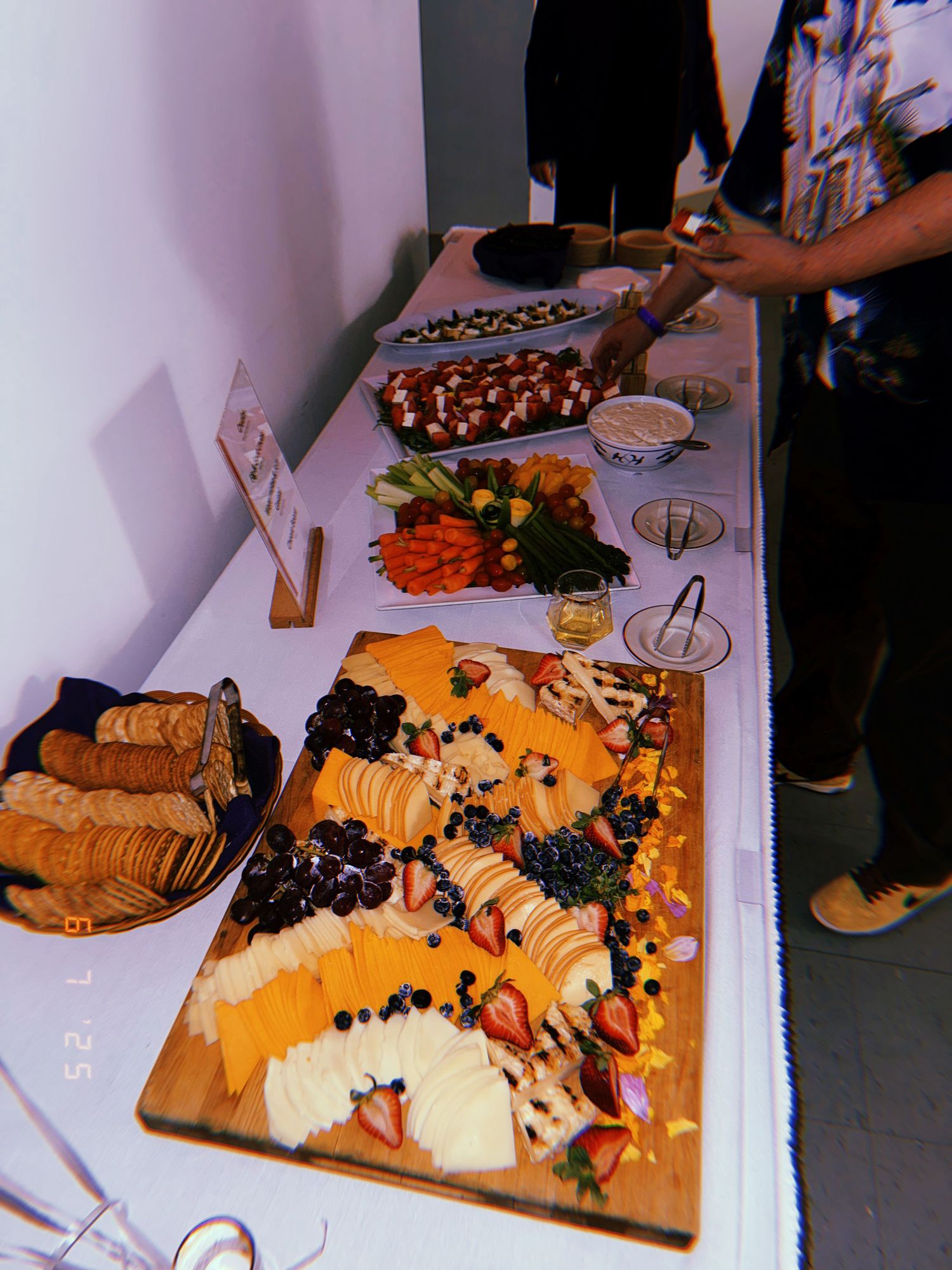A buffet table with cheese and charcuterie boards, fresh vegetables, spring rolls and appetizers arranged on white linens.