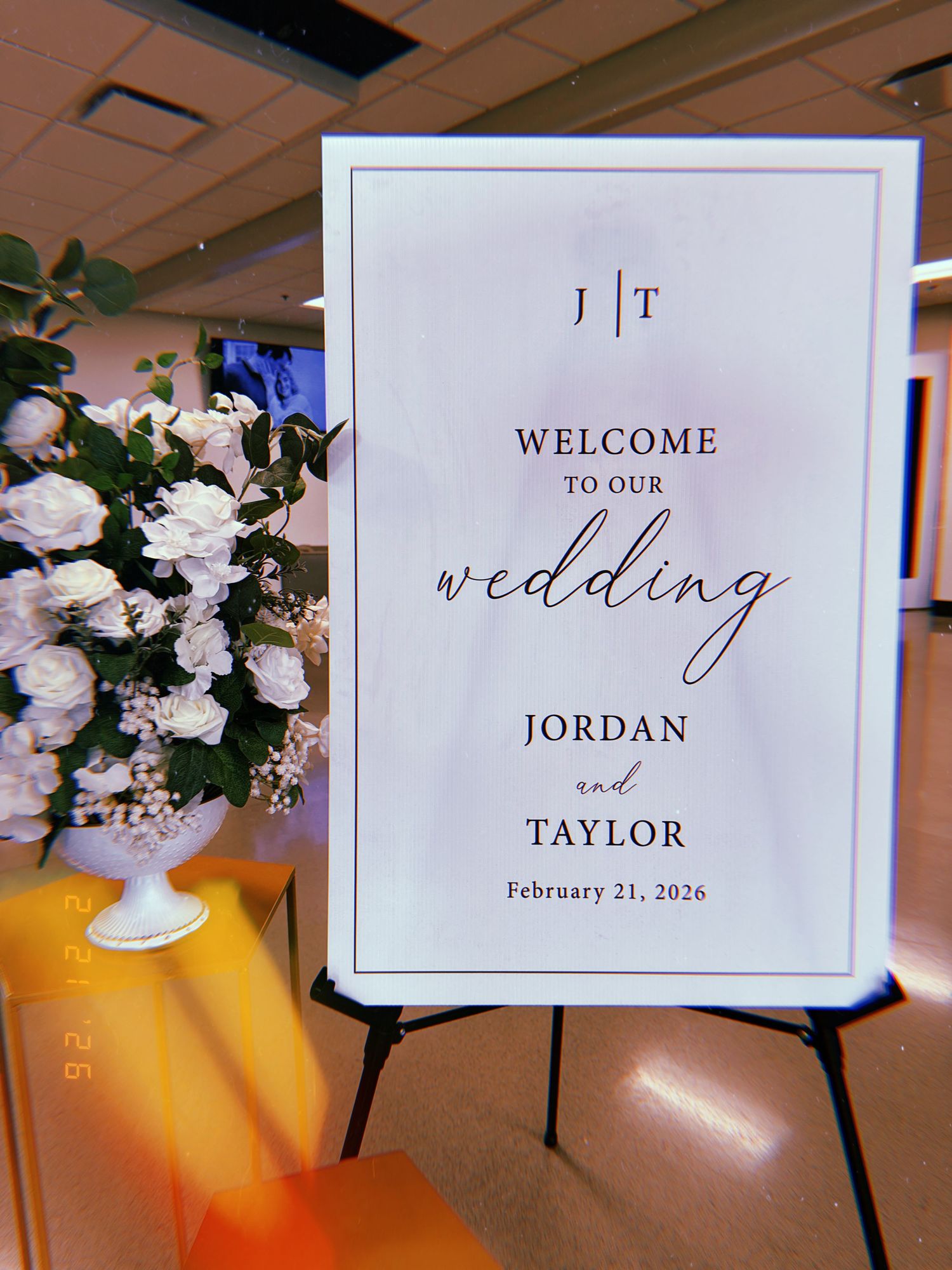 An elegant wedding welcome sign with floral arrangement displays 'Jordan and Taylor' with the date February 21, 2020.
