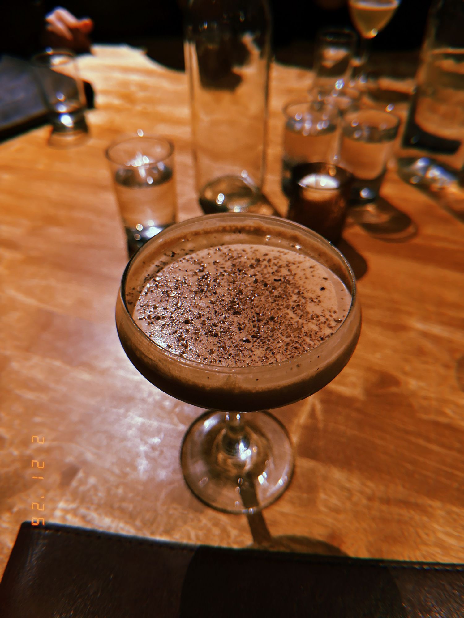 A sequence of chocolate martinis garnished with cocoa powder served in elegant cocktail glasses on a wooden bar top.