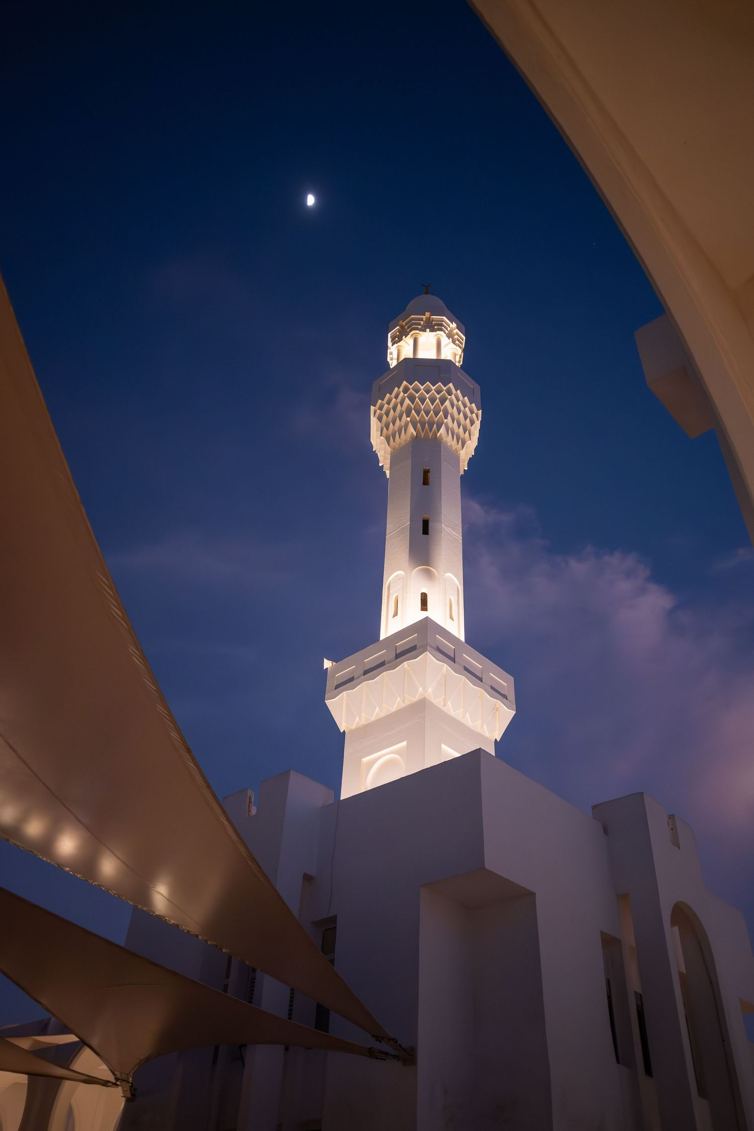White lighthouse tower against deep blue evening sky photographed from below in a creative architectural composition.