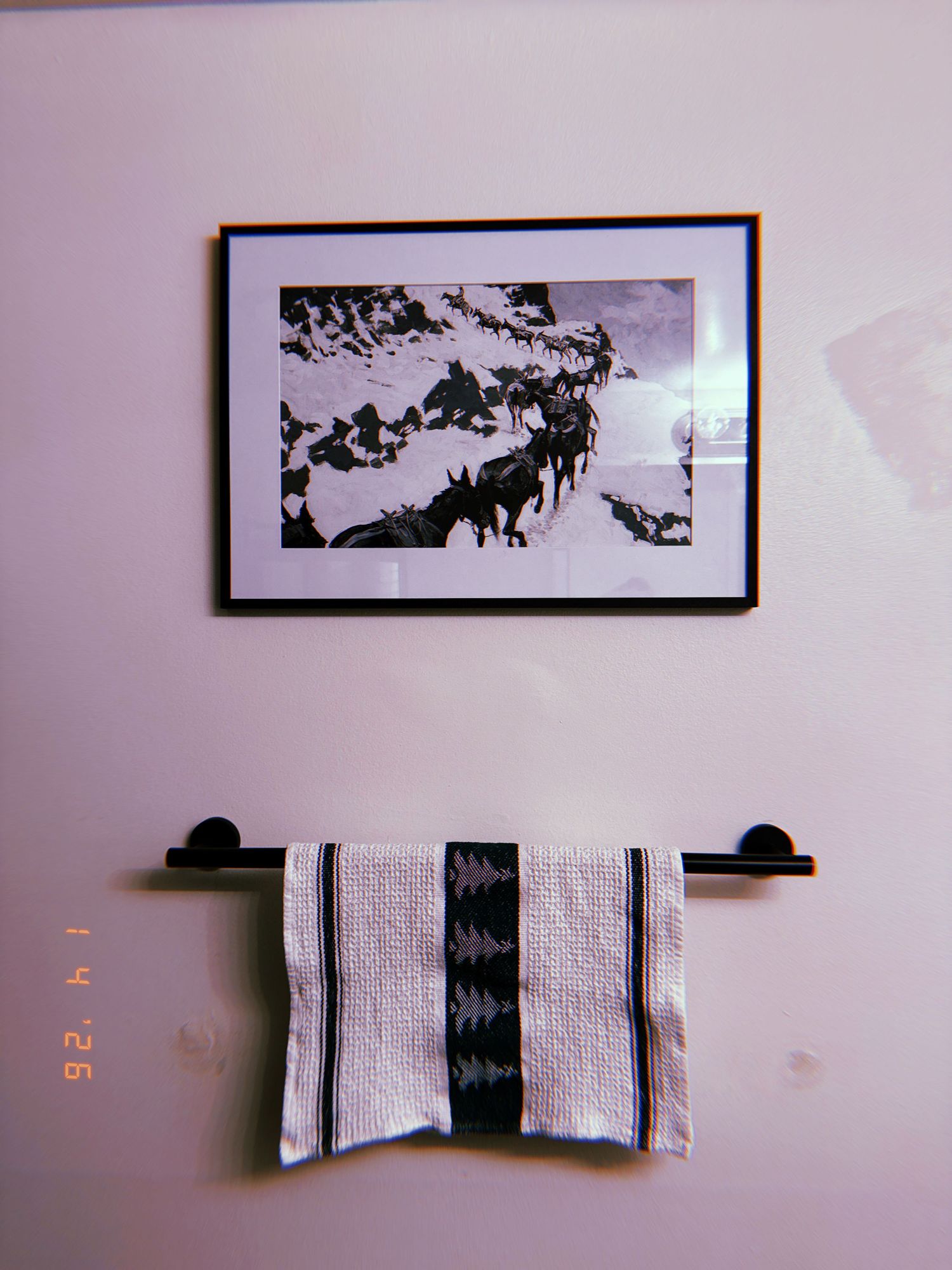 A series of six framed black and white photographs hanging on a white wall with a towel bar mounted below.