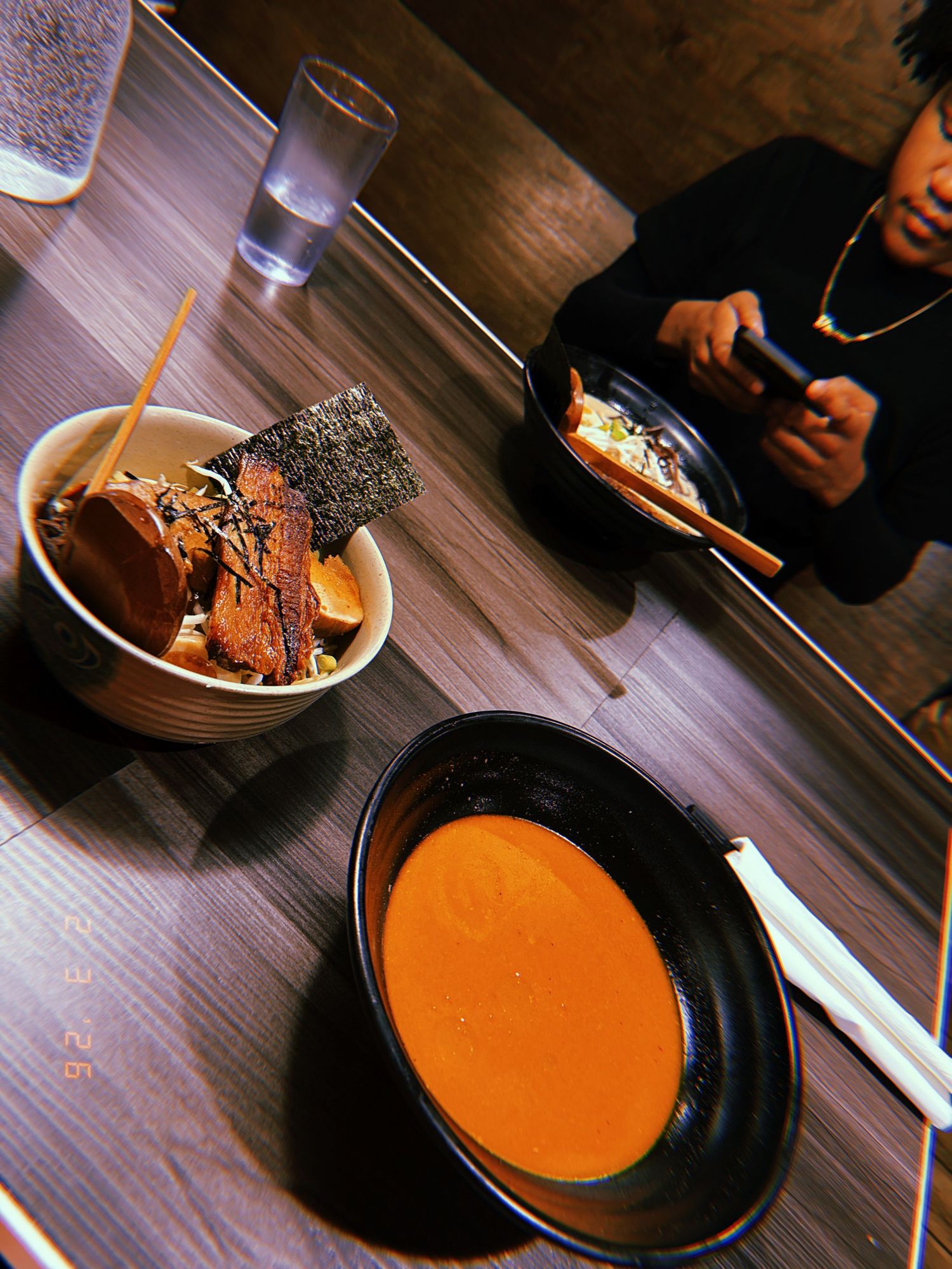 Japanese ramen bowls and orange soup served on a dark wooden table with chopsticks and drinks.