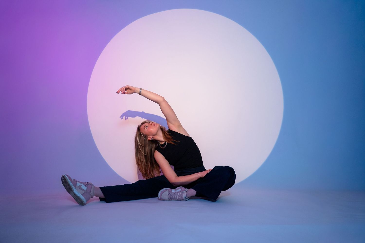 Graceful dancer in black performs a fluid movement sequence against a purple and blue gradient backdrop.