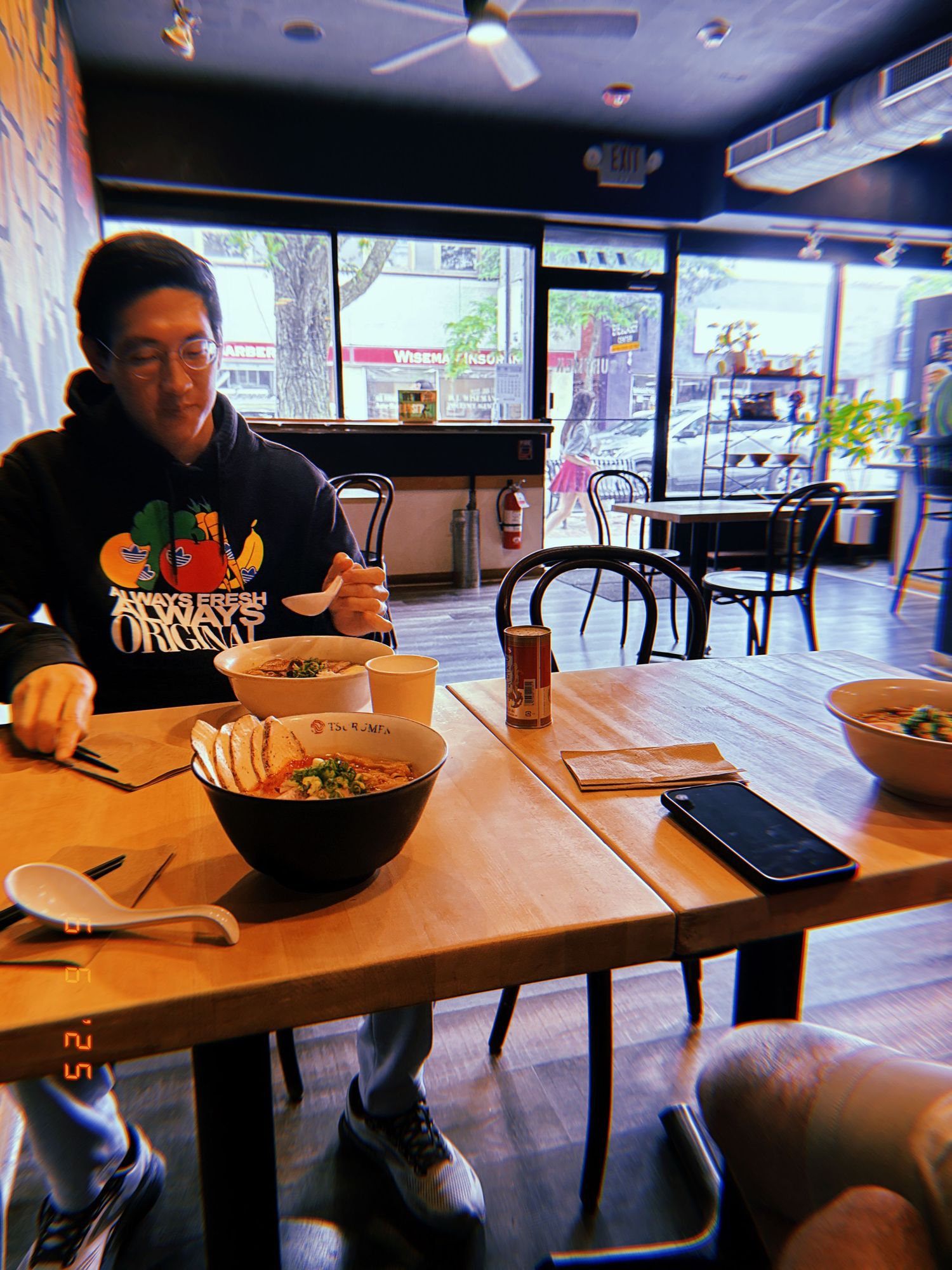 Someone dining alone at a casual restaurant with food in bowls and drinks on a wooden table in a dimly lit interior.