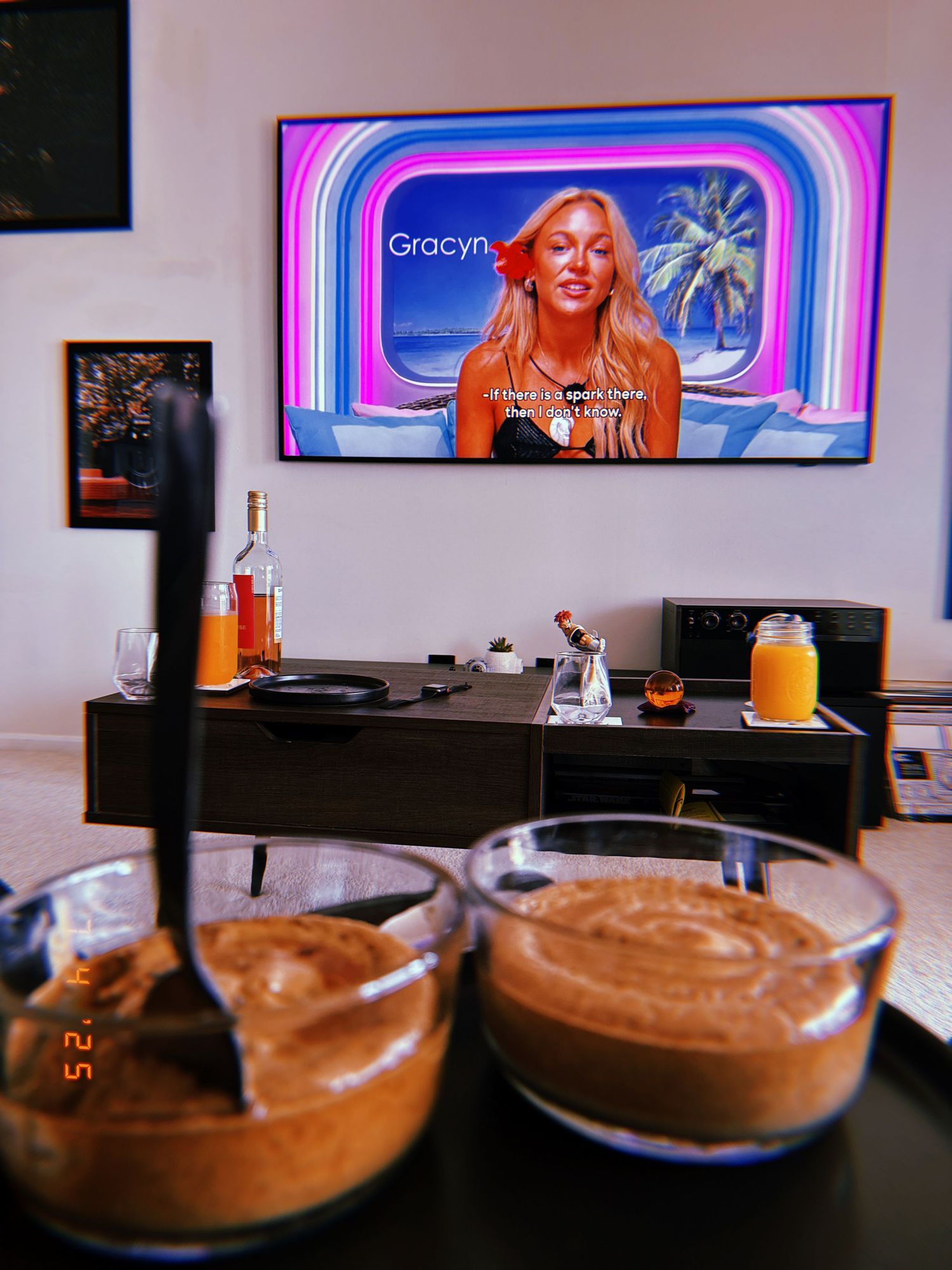 Chocolate smoothies in glasses on a counter with a TV screen displaying colorful graphics in the background.