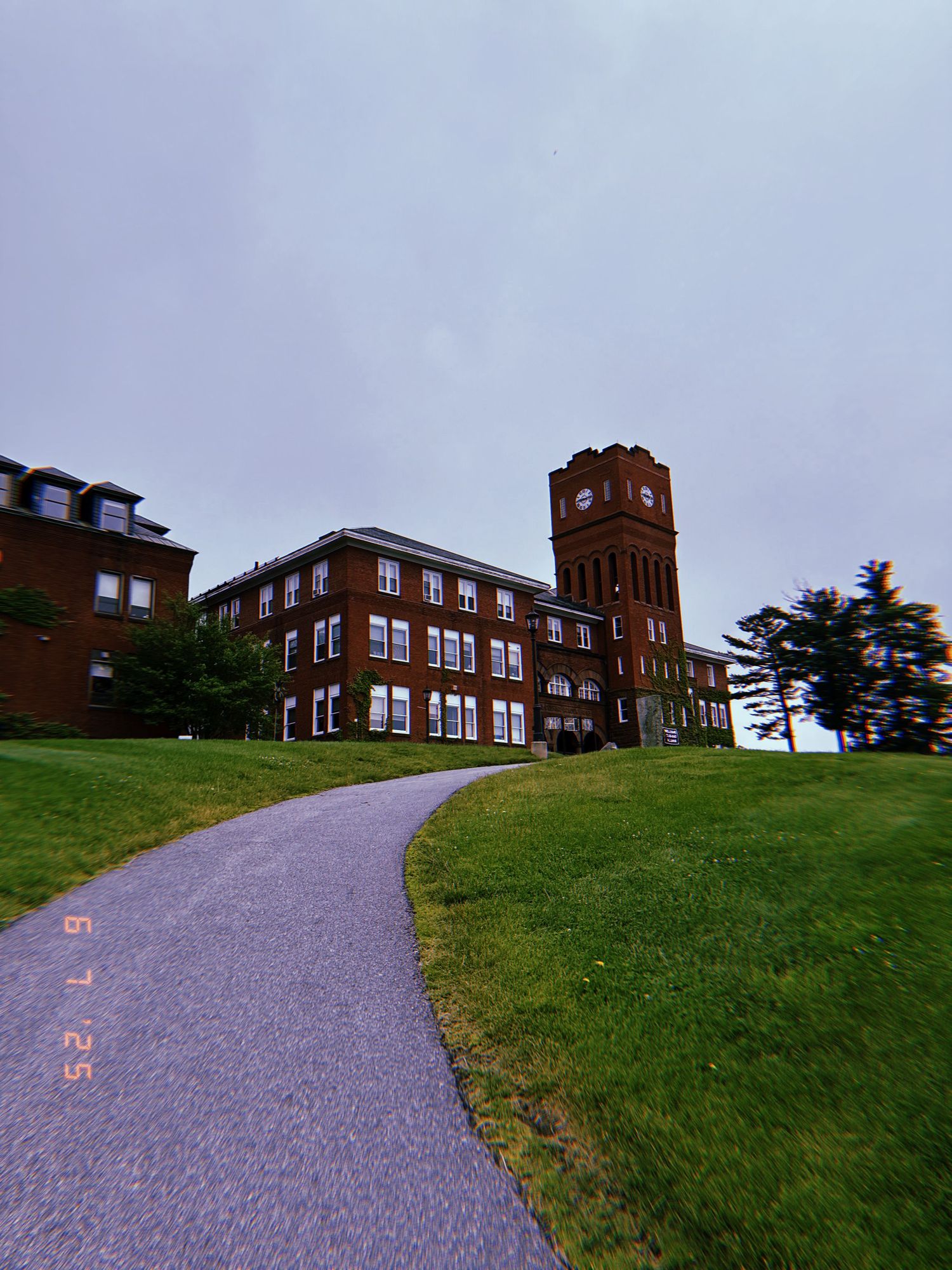 Winding paved pathway leading up to a historic brick school building on a grassy hilltop.