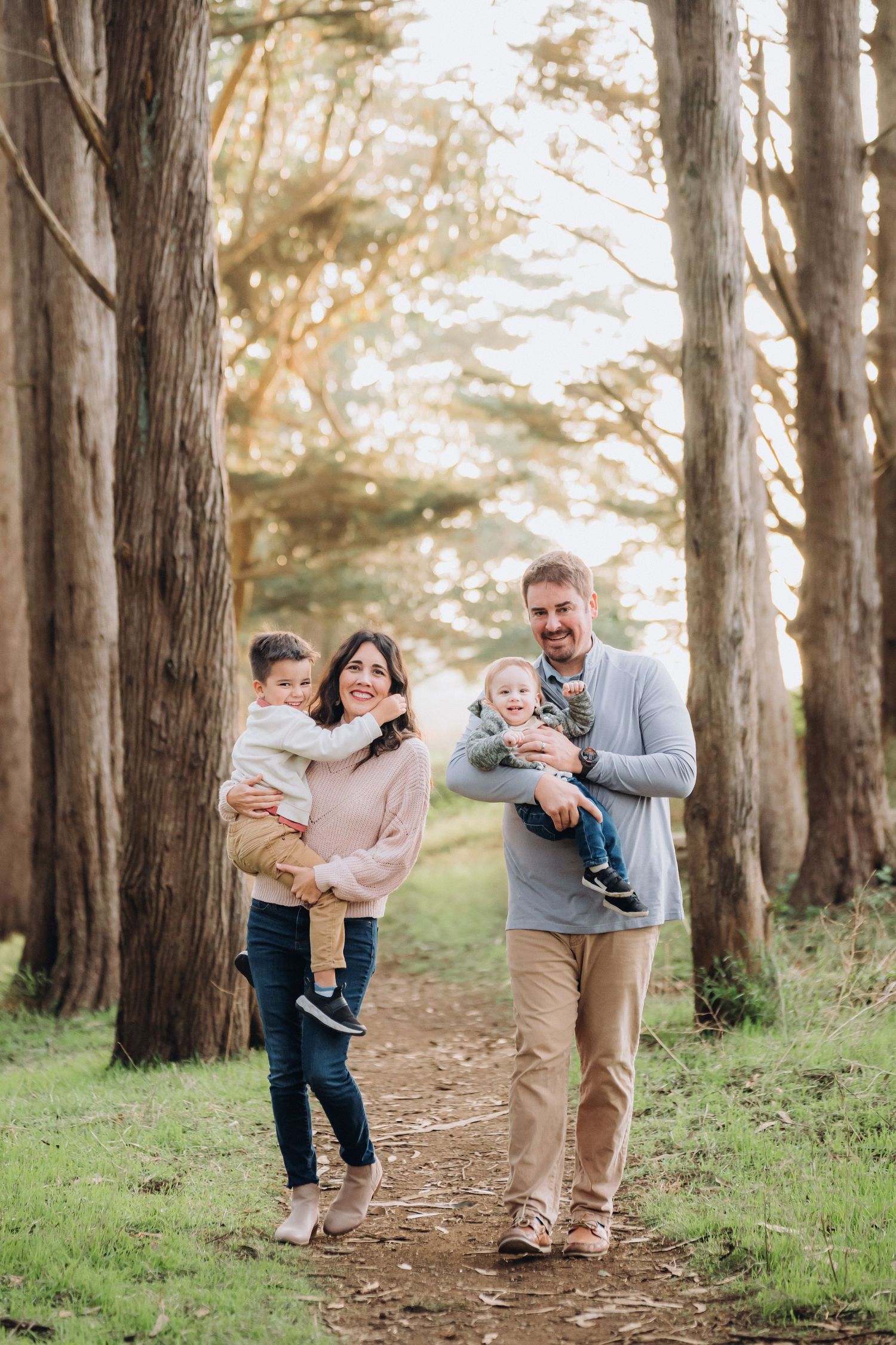 A family shares joyful moments together while walking along a scenic tree-lined path in golden afternoon light.