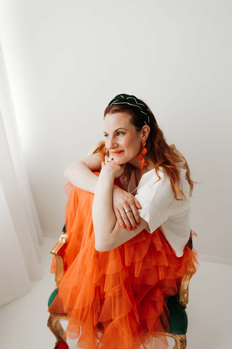 Fashion portrait of a person in a flowing orange tulle dress posing against a white backdrop.