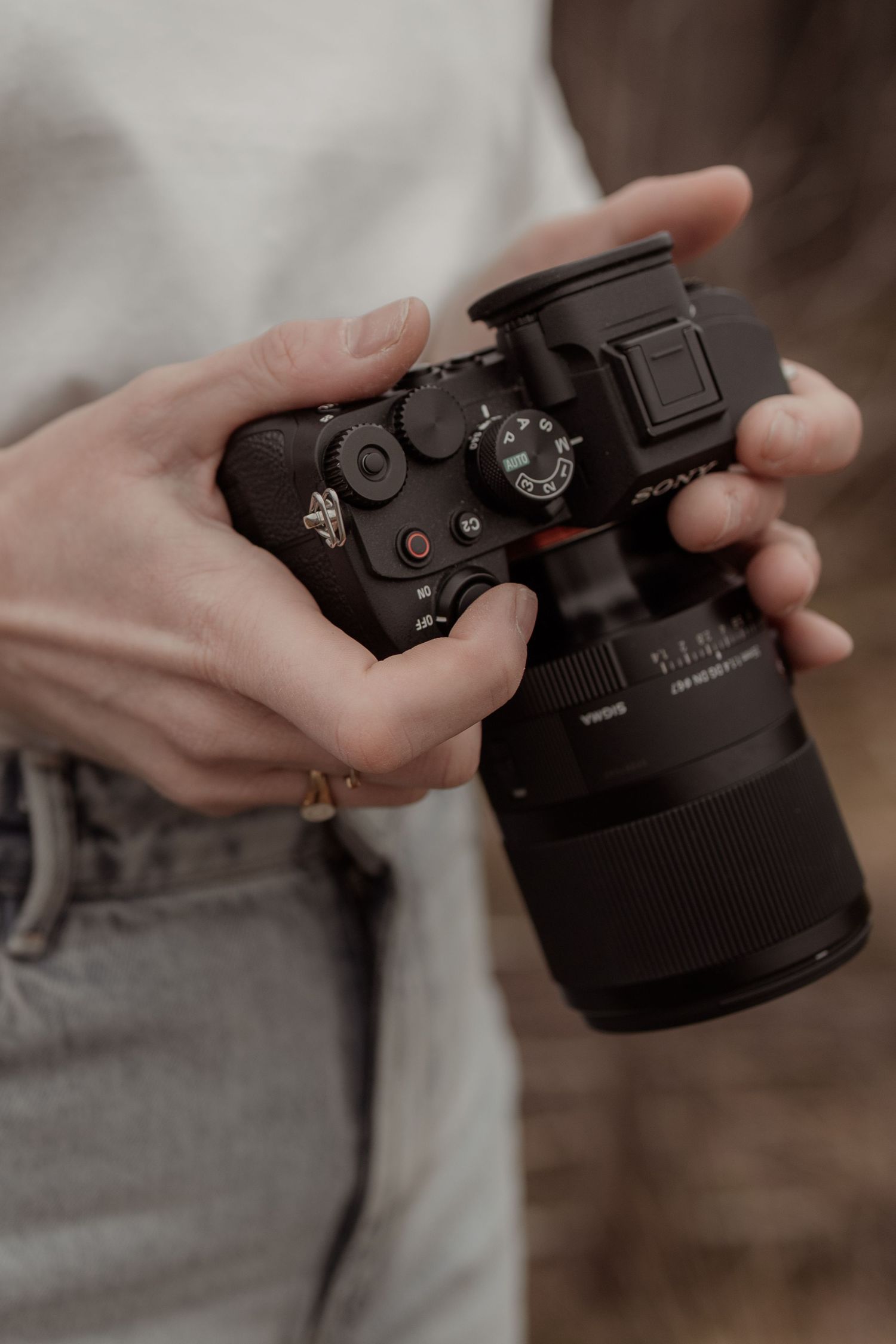 Close-up view of hands adjusting settings on a black digital camera lens in natural lighting.