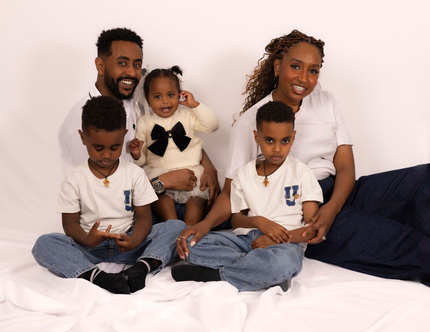 familjefoto, en mamma och en pappa med deras tre barn sitter i en studio tillsammans. på sig har de jeans och vita t-shirtar