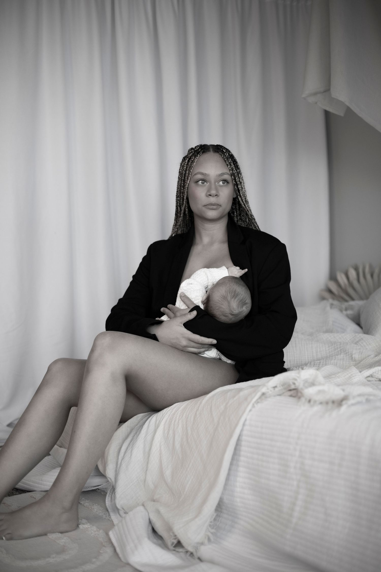 mamma sitter på sängkanten med sitt barn i famnen och kollar utåt.
