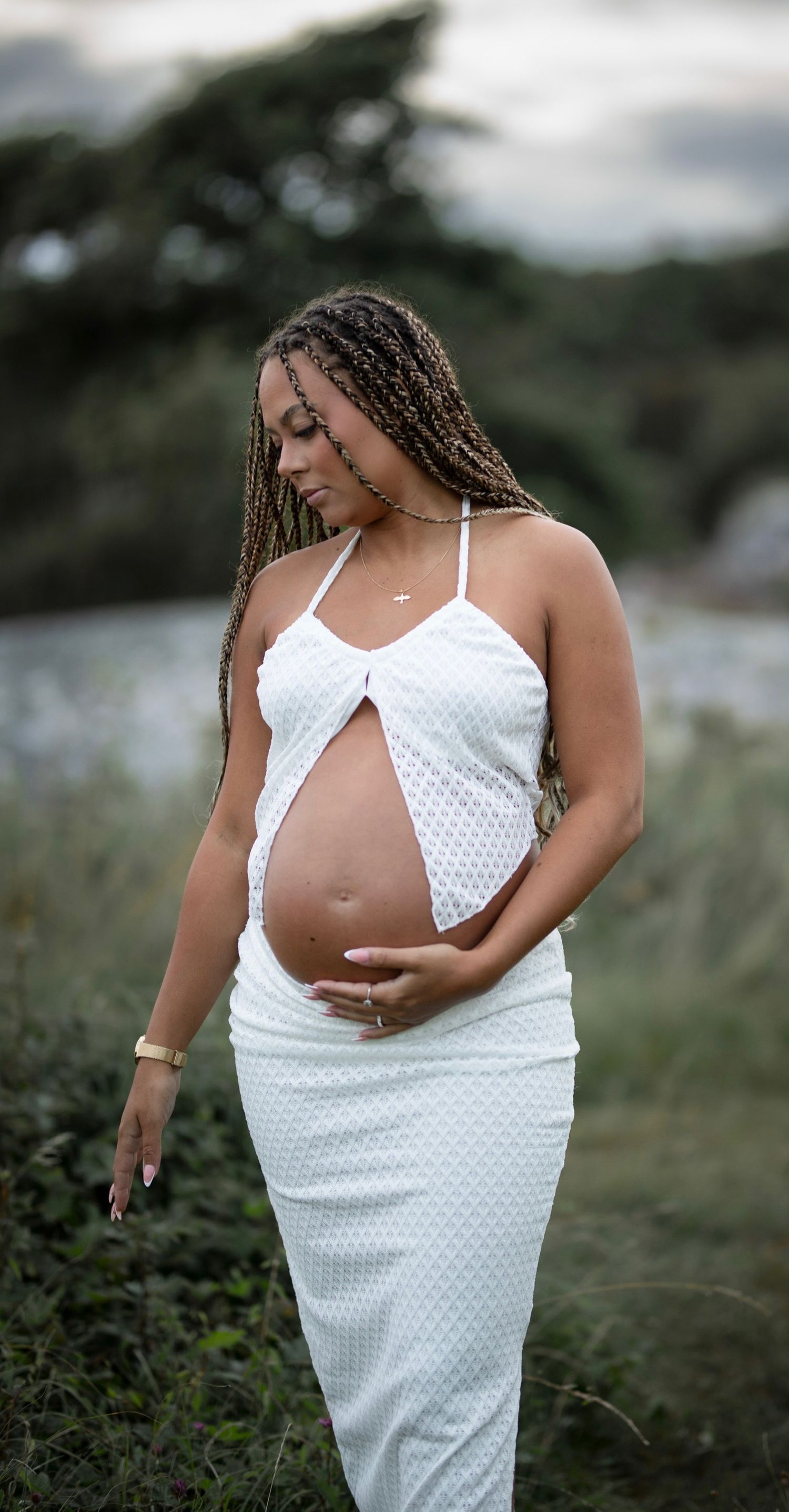 gravid kvinna står på en äng, hon kollar ner i marken. hon har ett vitt set på sig.