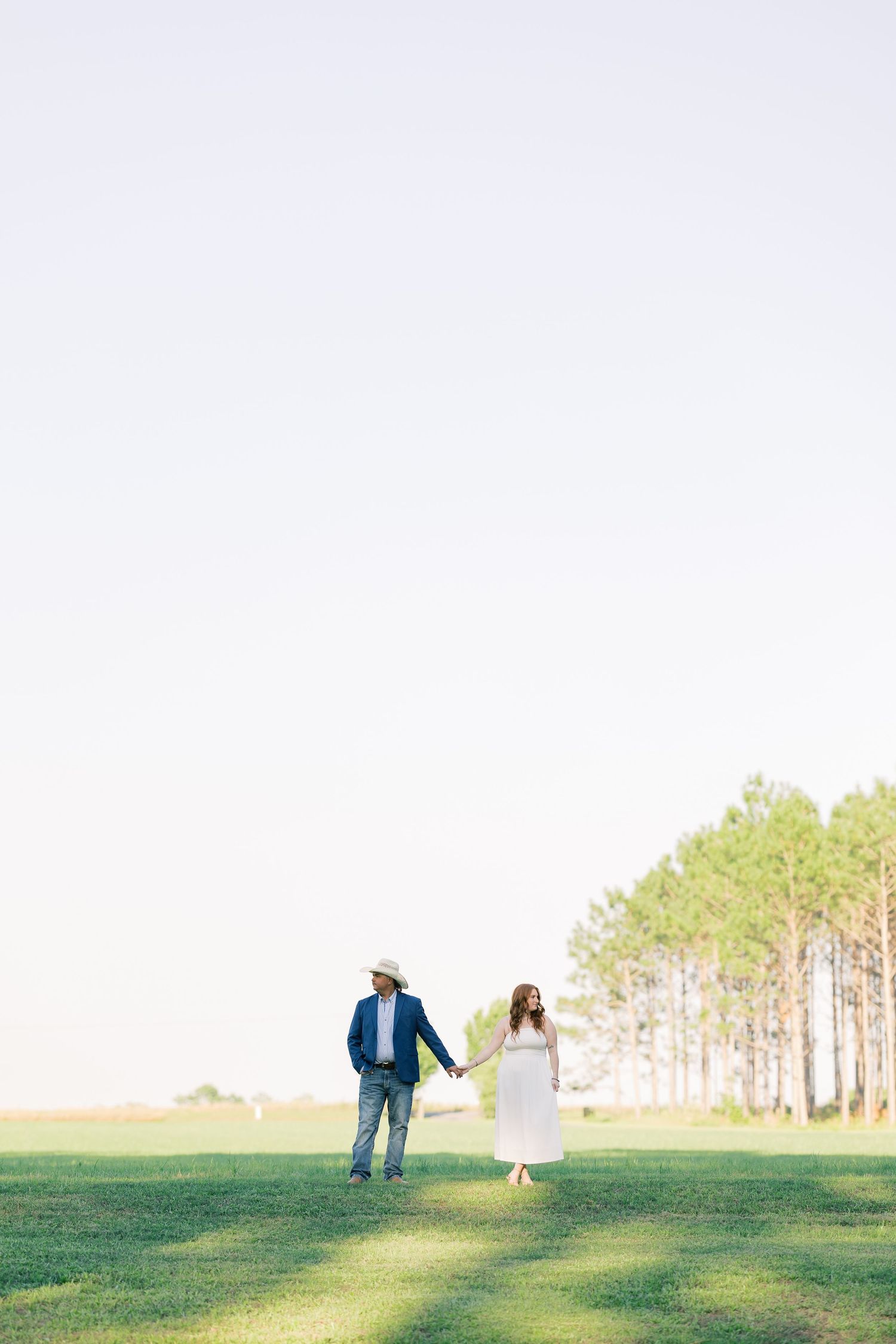 A couple holding hands while walking across a lush green field under a bright open sky.