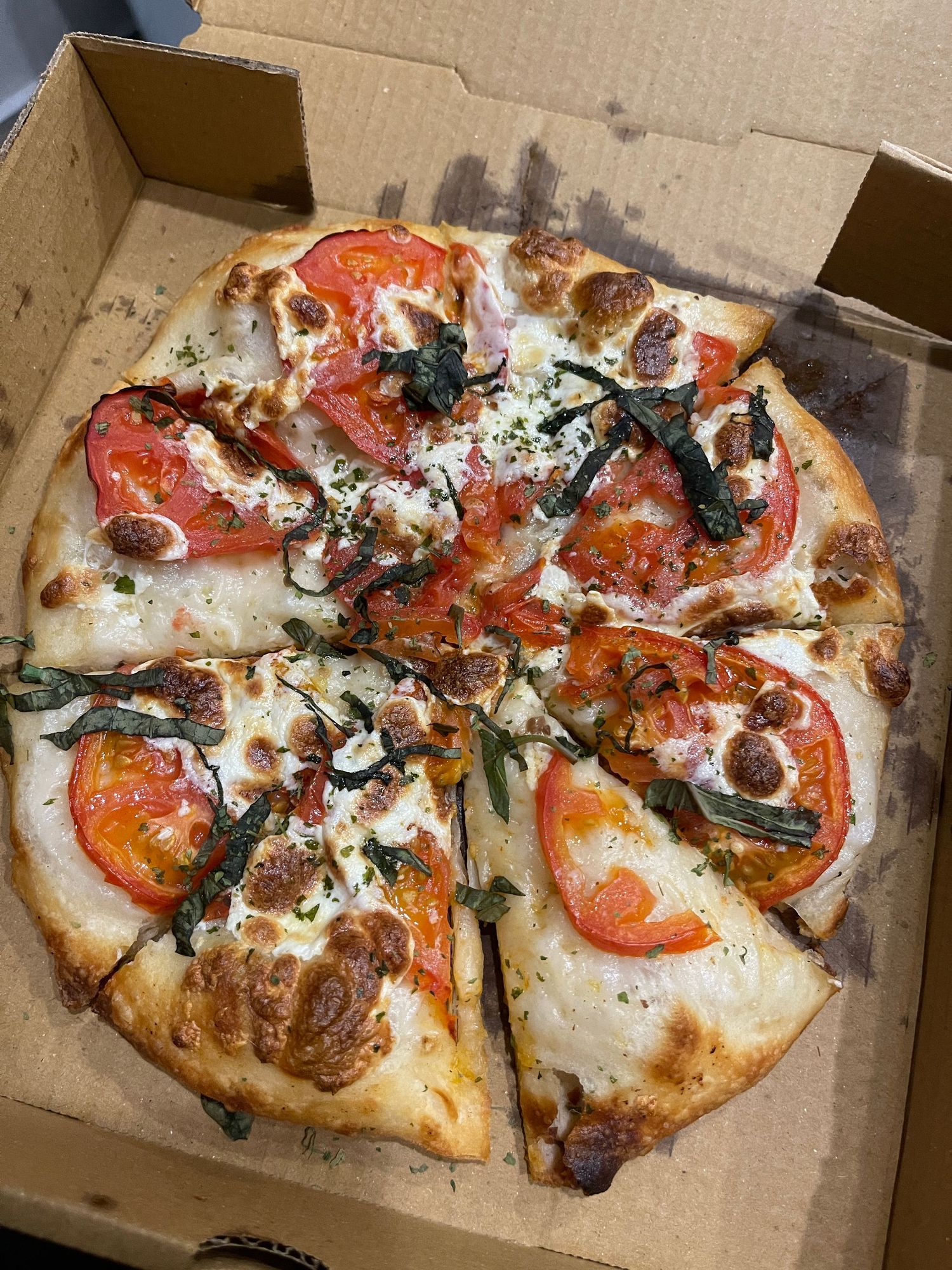 A freshly baked tomato and basil pizza with melted mozzarella cheese in an open cardboard box.