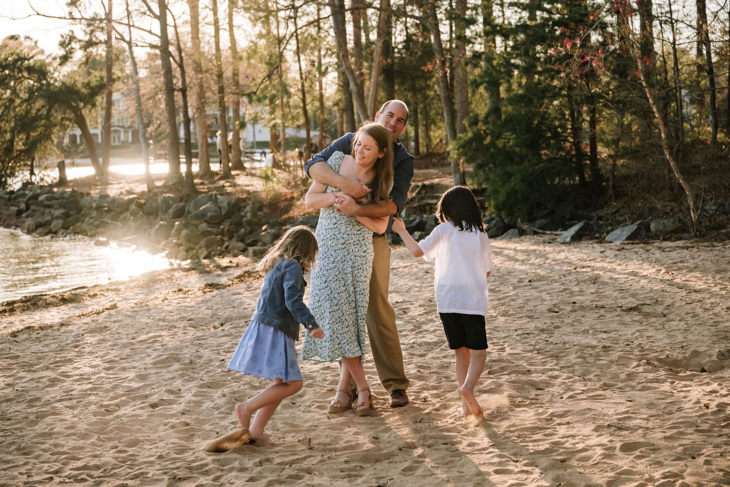 A joyful family plays together on a sandy beach at sunset with sunlight streaming through the trees.
