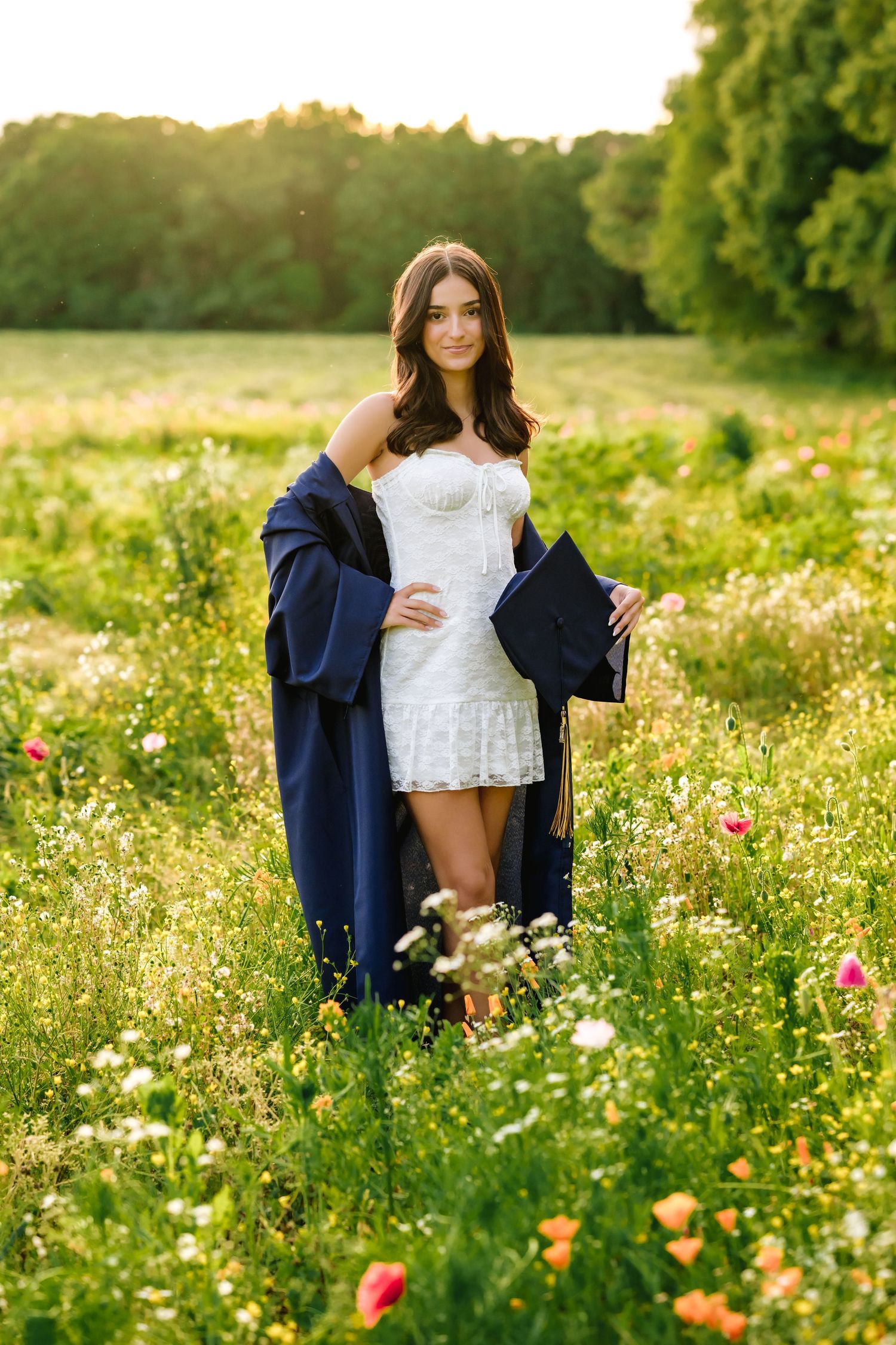 Person sitting in a field of wildflowers during sunset wearing a white top and navy jacket.