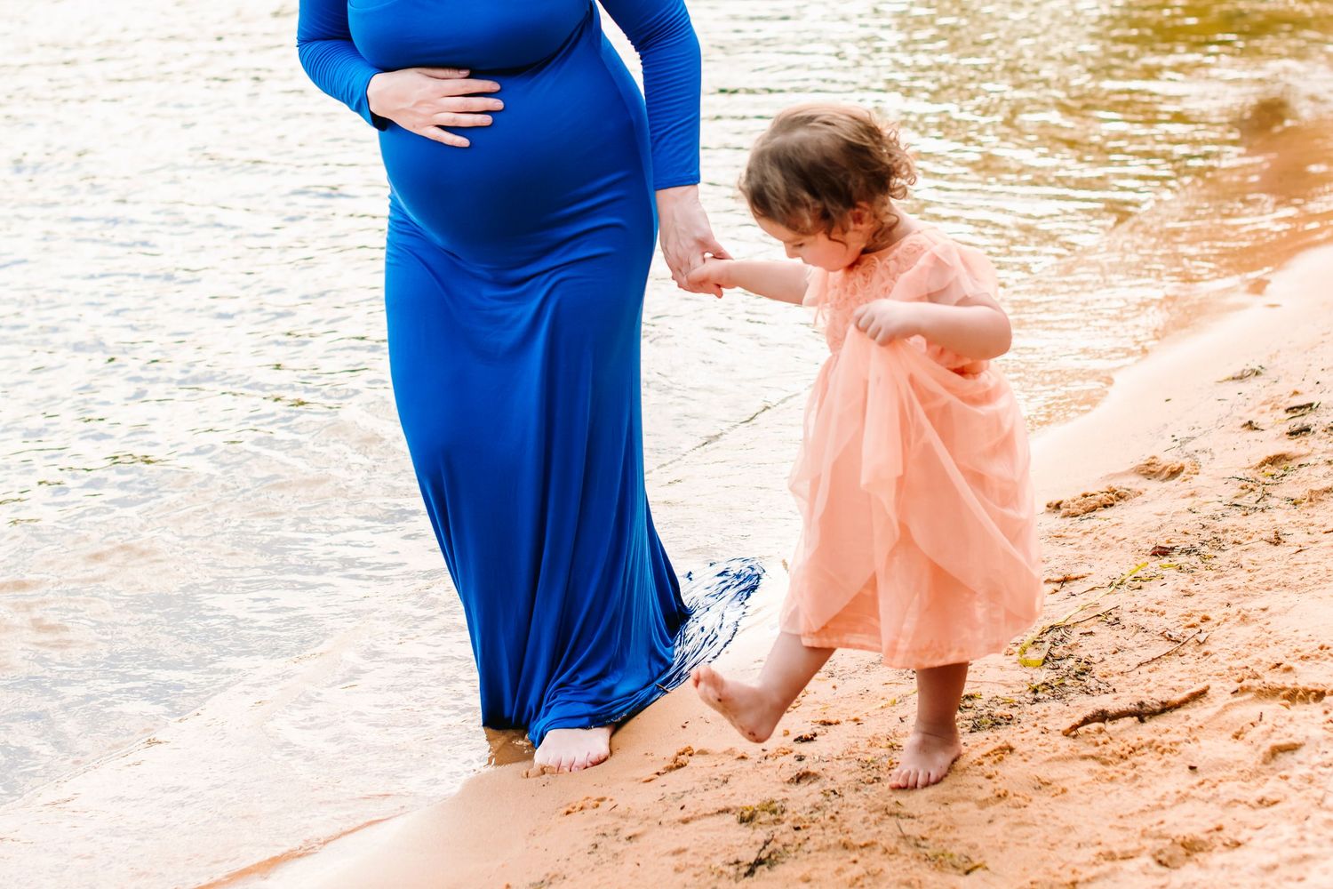 Mother and daughter in blue and pink outfits play together on a beach at sunset.