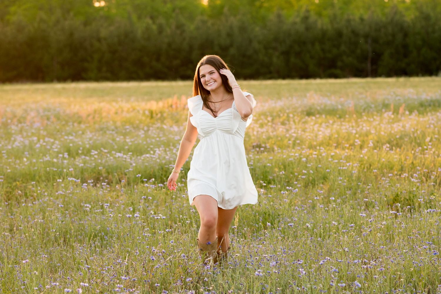Young woman in white dress walking through wildflower meadow at golden hour sunset.