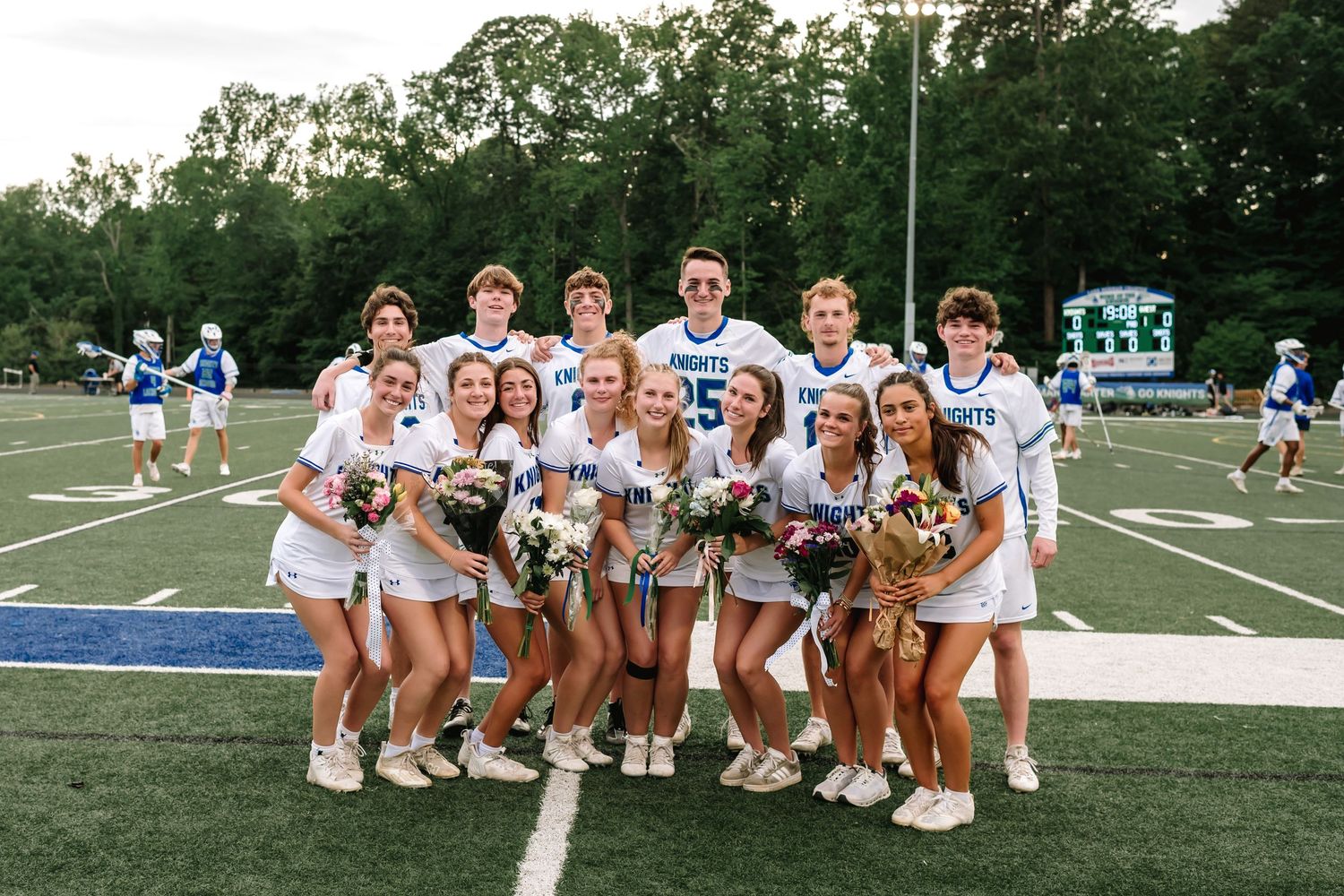 Cheerleaders in white uniforms pose together on football field during game day.
