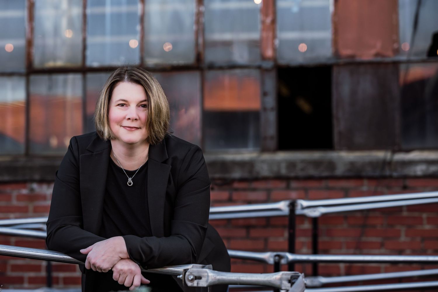Professional headshots in black blazer against urban background with string lights creating a warm ambiance.