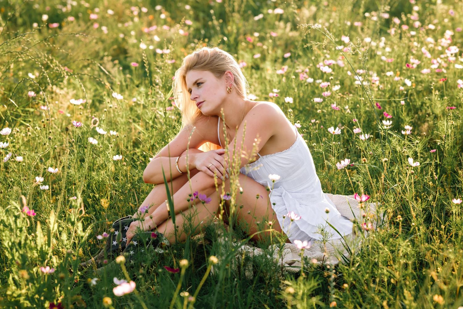 Person in white dress lying in a sunny meadow filled with wildflowers.