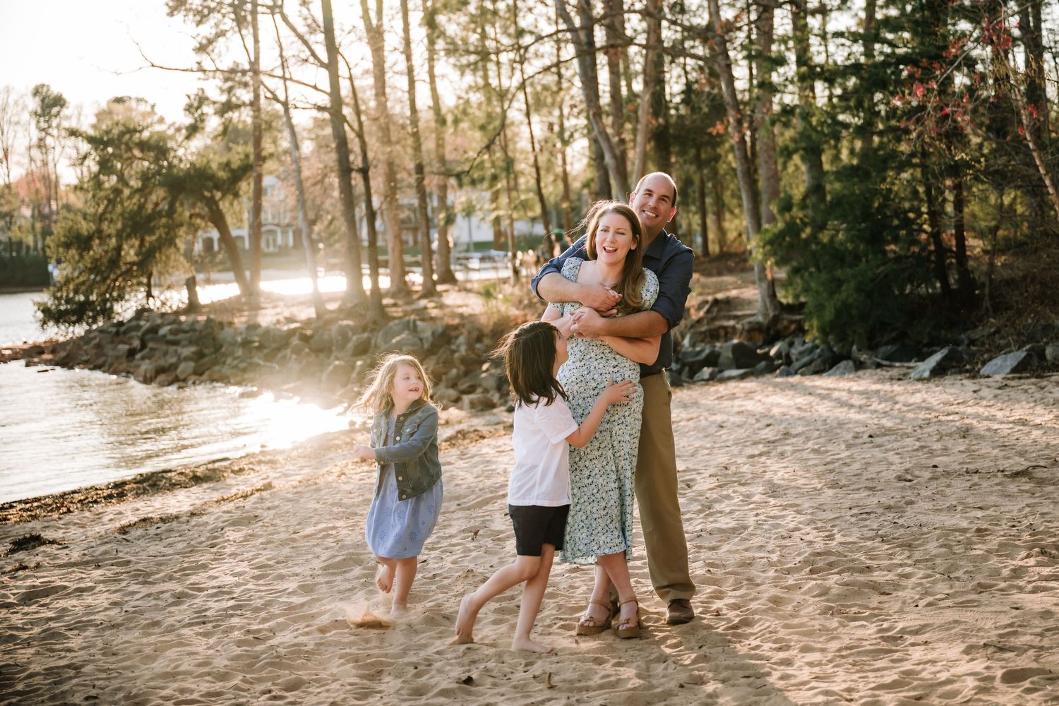 A family embraces on a sandy beach at sunset with trees in the background.
