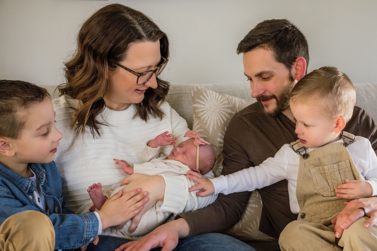 Family of five with newborn baby sitting together on a couch, parents and two young siblings smiling warmly.