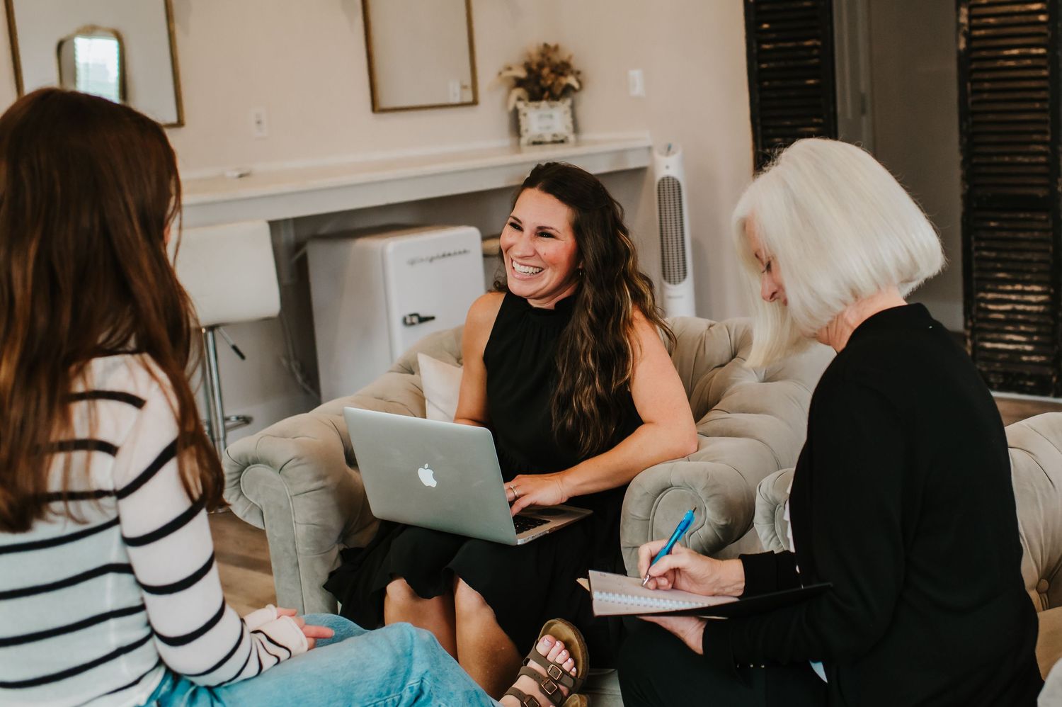 Three people having a casual meeting with laptops in a cozy living room setting.