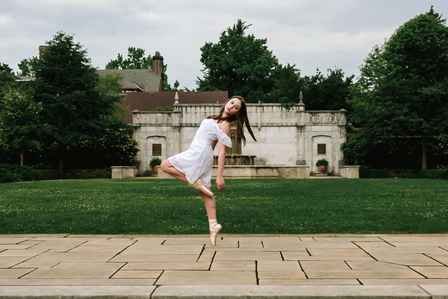 Figure in white dress leaping gracefully across stone pavers in a garden setting.